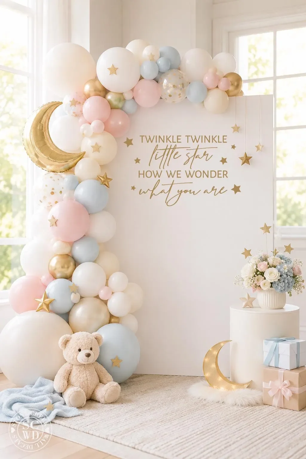Pastel baby shower backdrop with balloon garland, gold crescent moon, stars, and teddy bear.