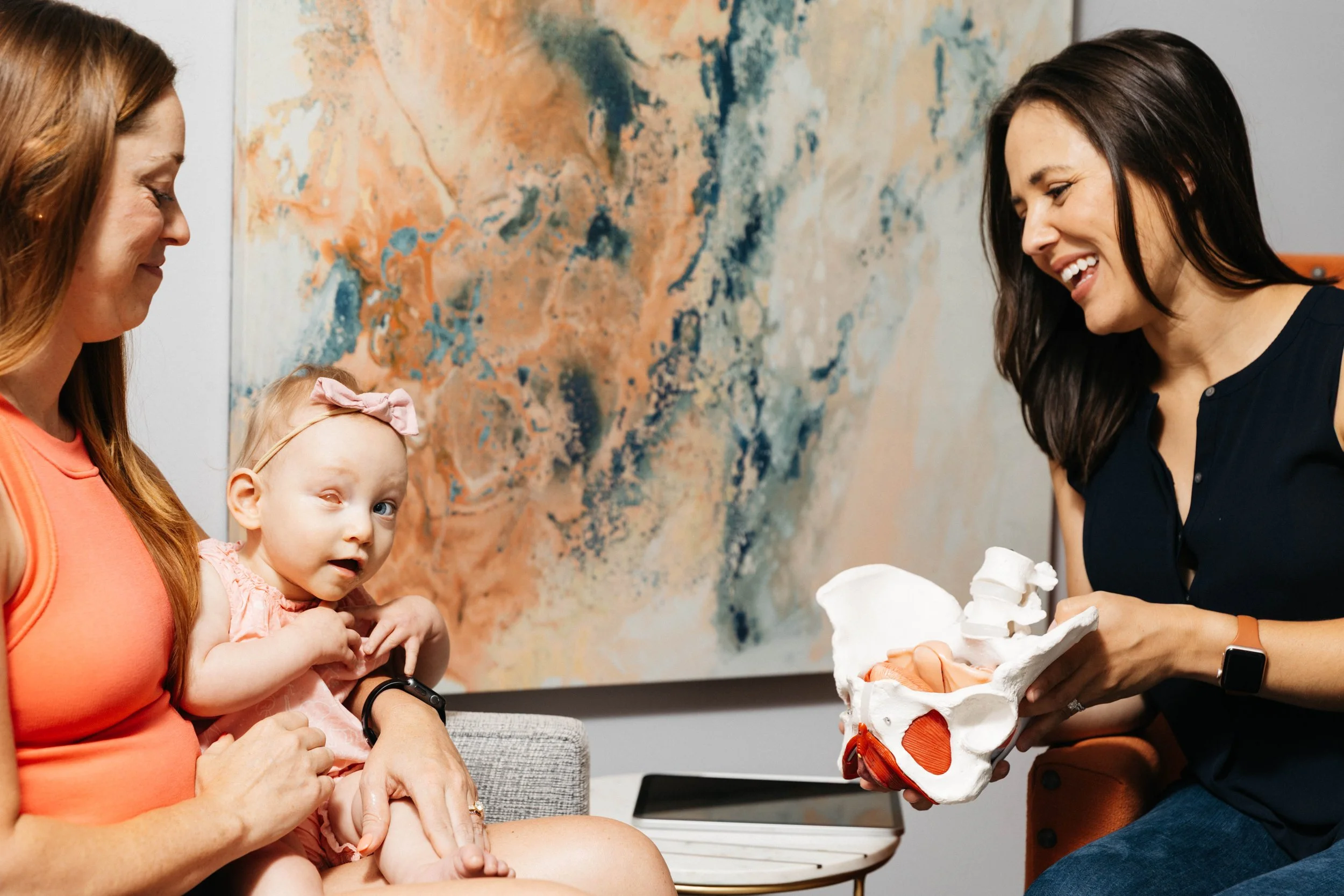 A pelvic floor therapist shows a pregnant woman and her daughter a pelvis model during a pelvic floor therapy session.