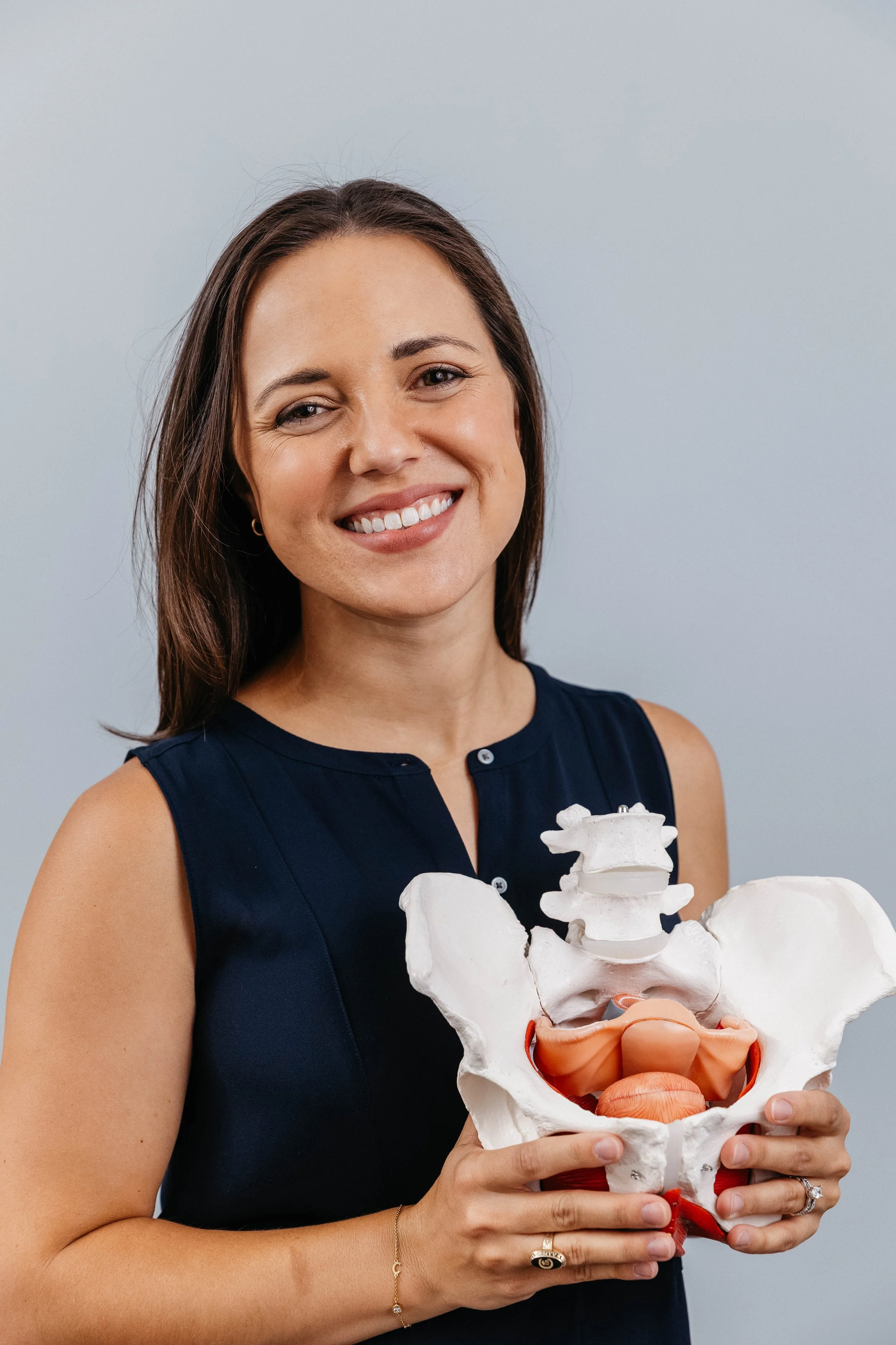 pelvic floor therapist holds pelvis to highlight importance of education and body awareness for recovery in postpartum, treating incontinence, painful sex, and constipation