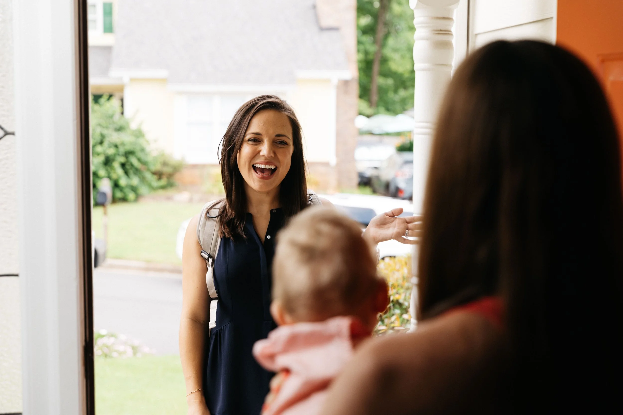 A pelvic floor therapist standing outside the door of her newly postpartum mom's home, arriving for a in-home pelvic floor therapy session to help with postpartum recovery.