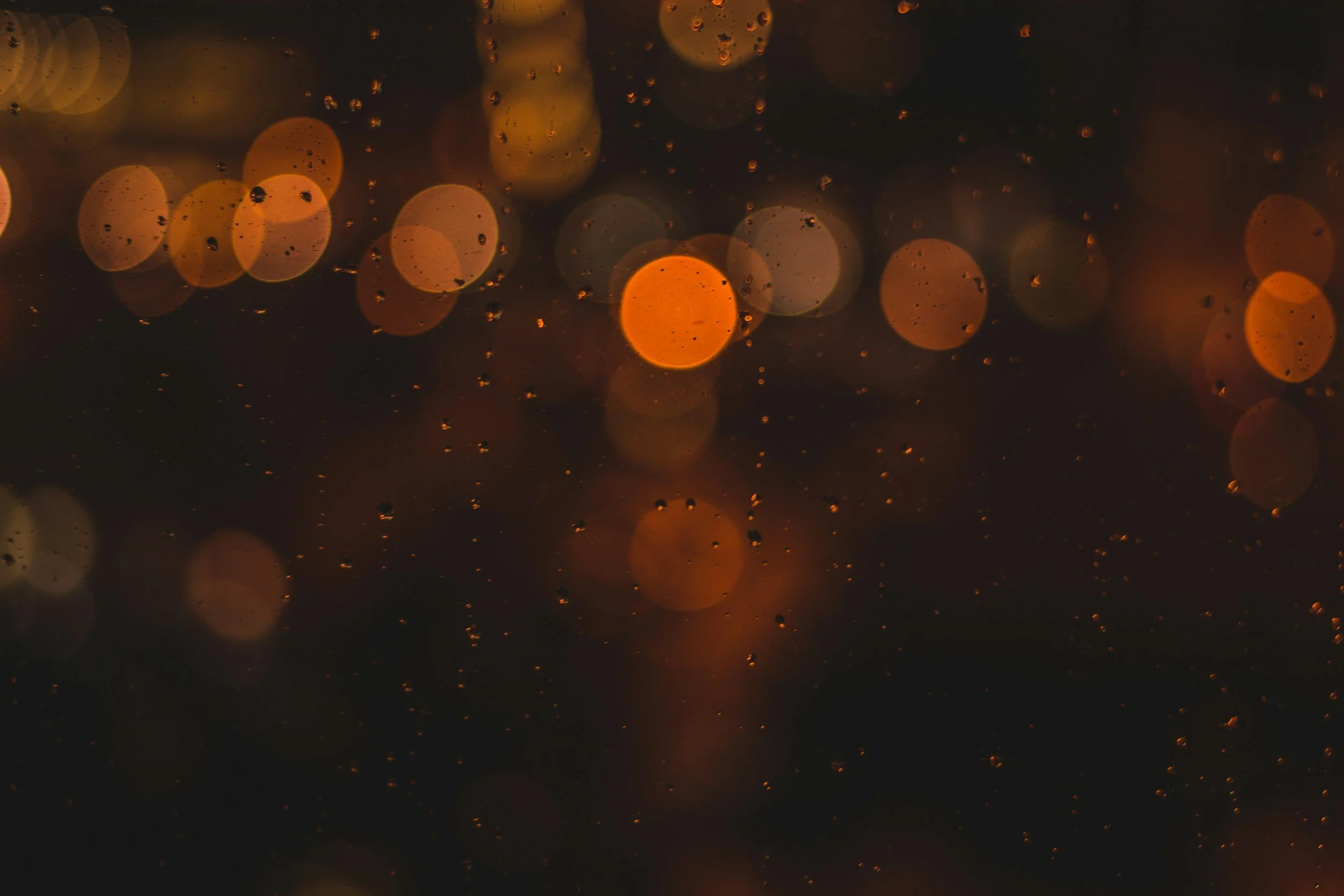 Blurred orange and white bokeh lights with raindrops on glass in the foreground.