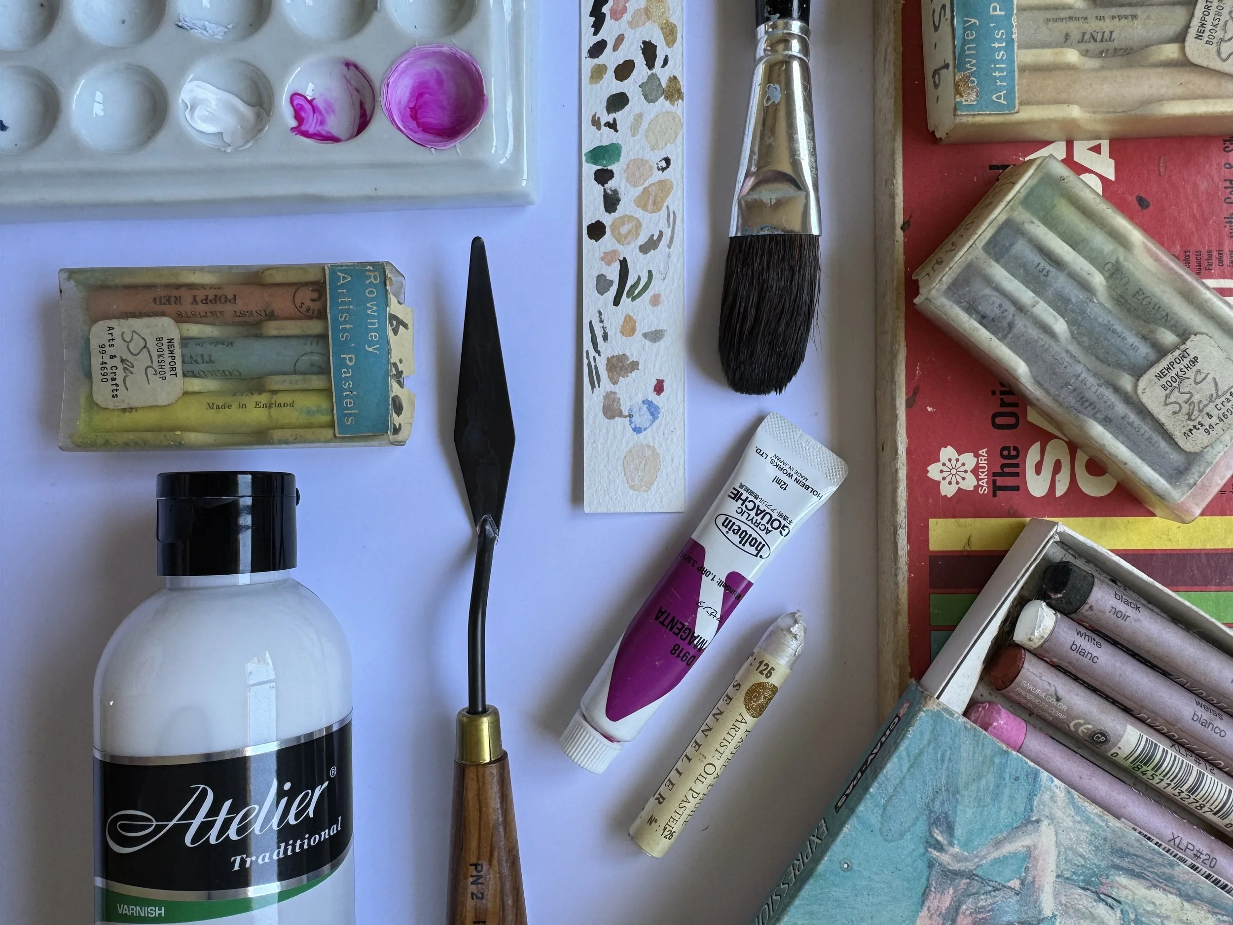 Artist's palette with pink and purple paint, various paint tubes, a paintbrush, a bottle of varnish, and art supplies on a white surface.