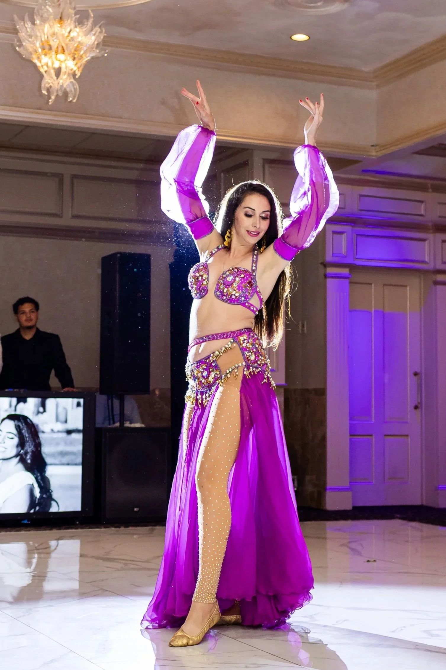 A belly dancer in a purple outfit is dancing at Il Tulipano at a wedding reception. 