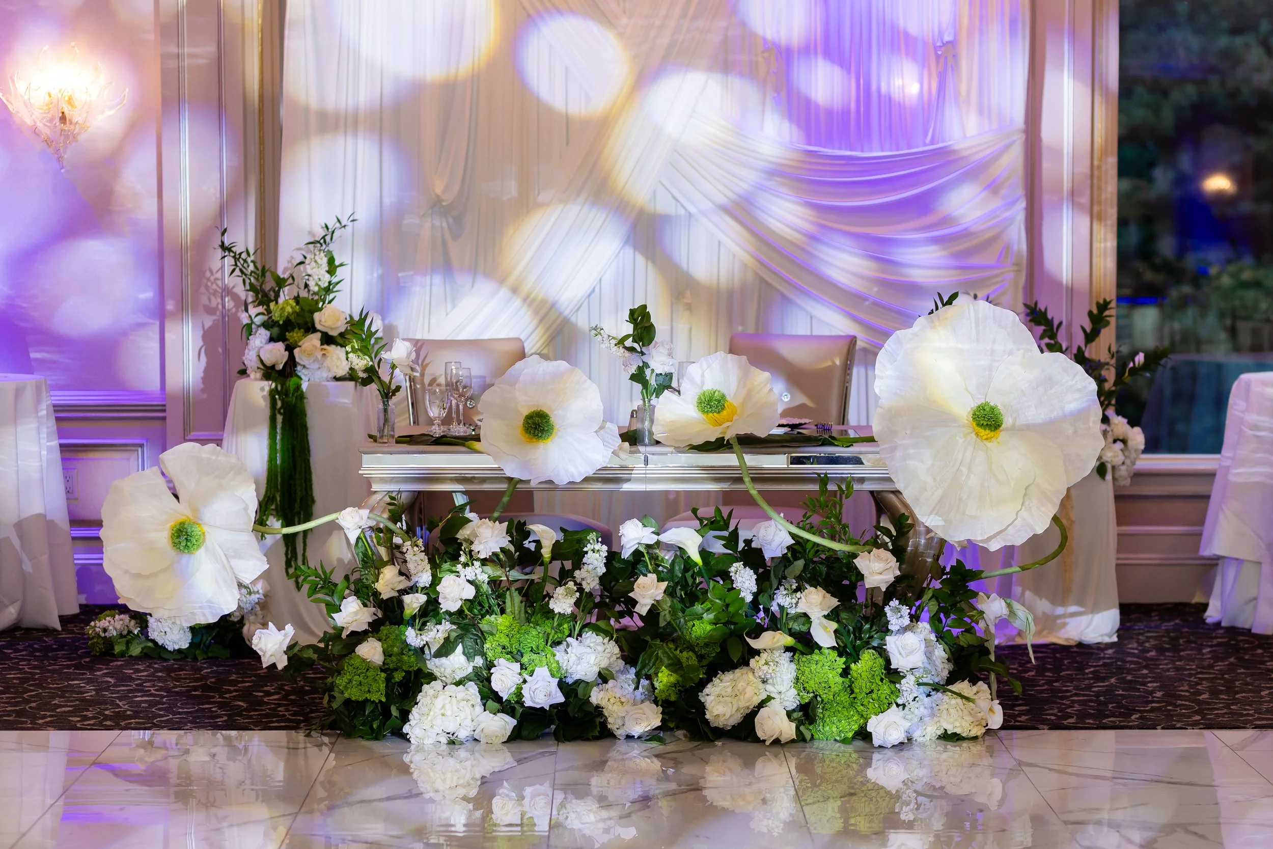 Whimsical fairytale sweetheart table decor with white florals and greenery with 4 large 3ft white flowers winding around the table at Il Tulipano in New Jersey.