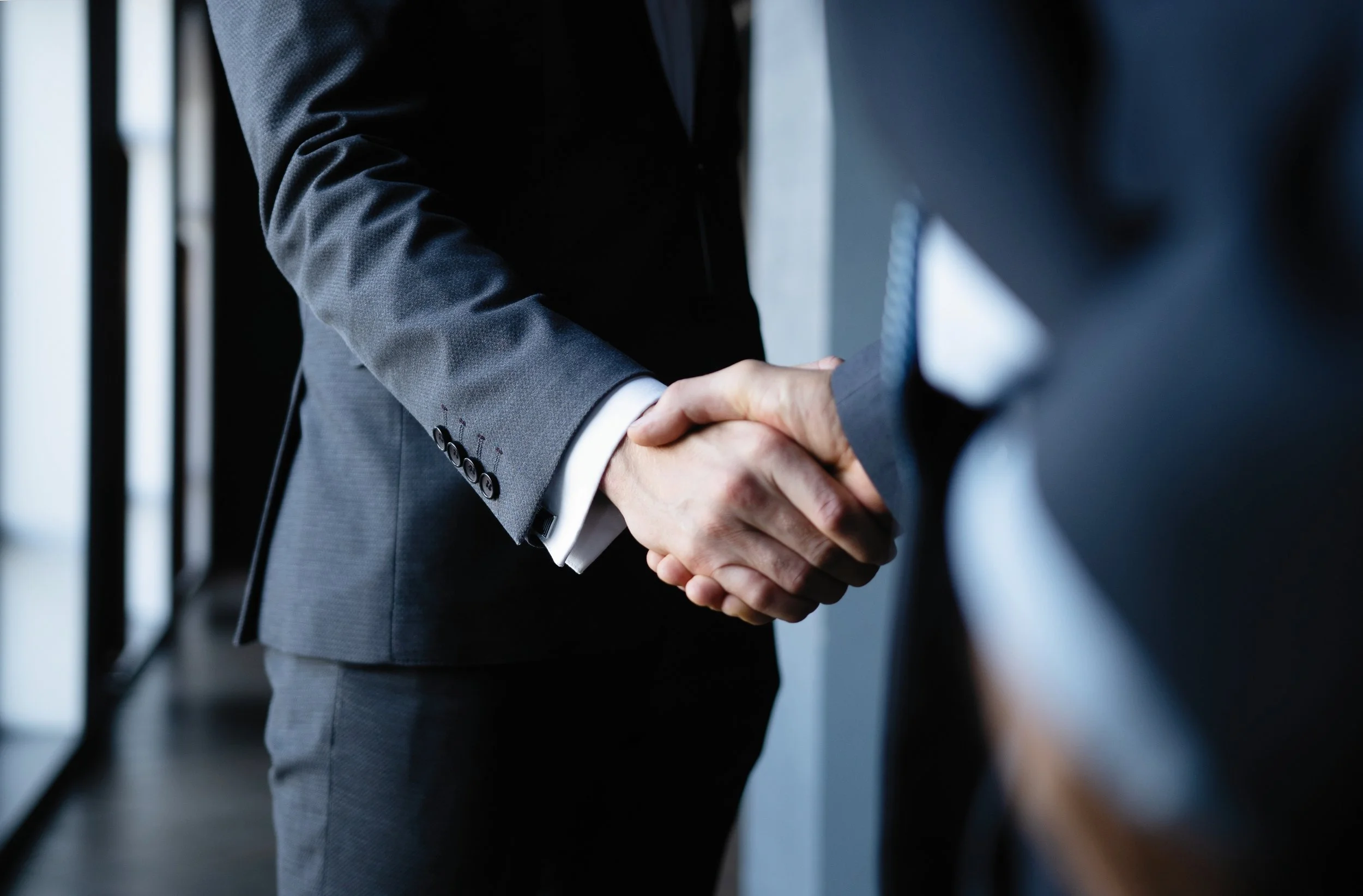 Close-up of two people in business suits shaking hands.