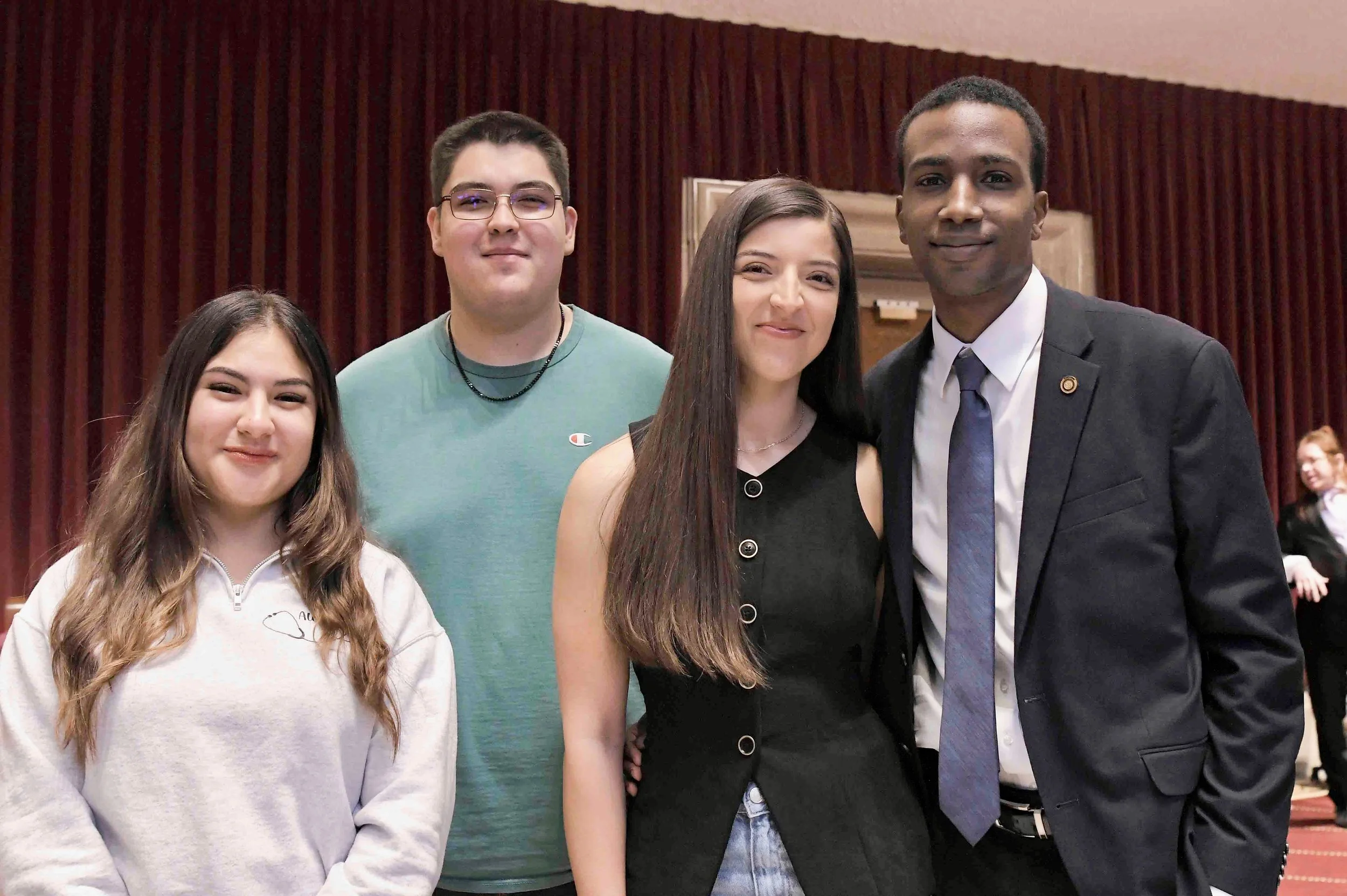 Group of four young adults standing indoors in front of a wooden wall, posing for a photo.