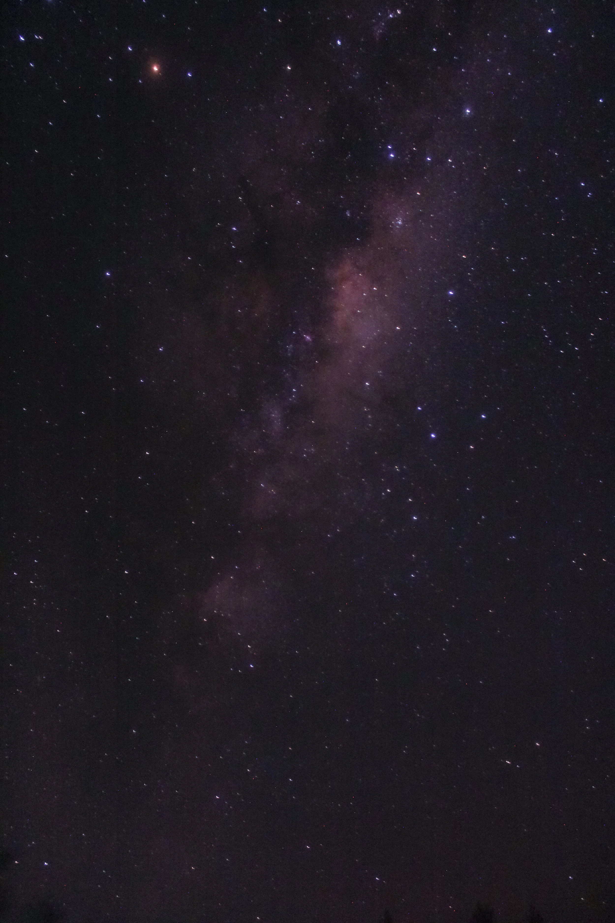 A clear night sky showing numerous stars and the Milky Way galaxy with a faint, reddish glow.
