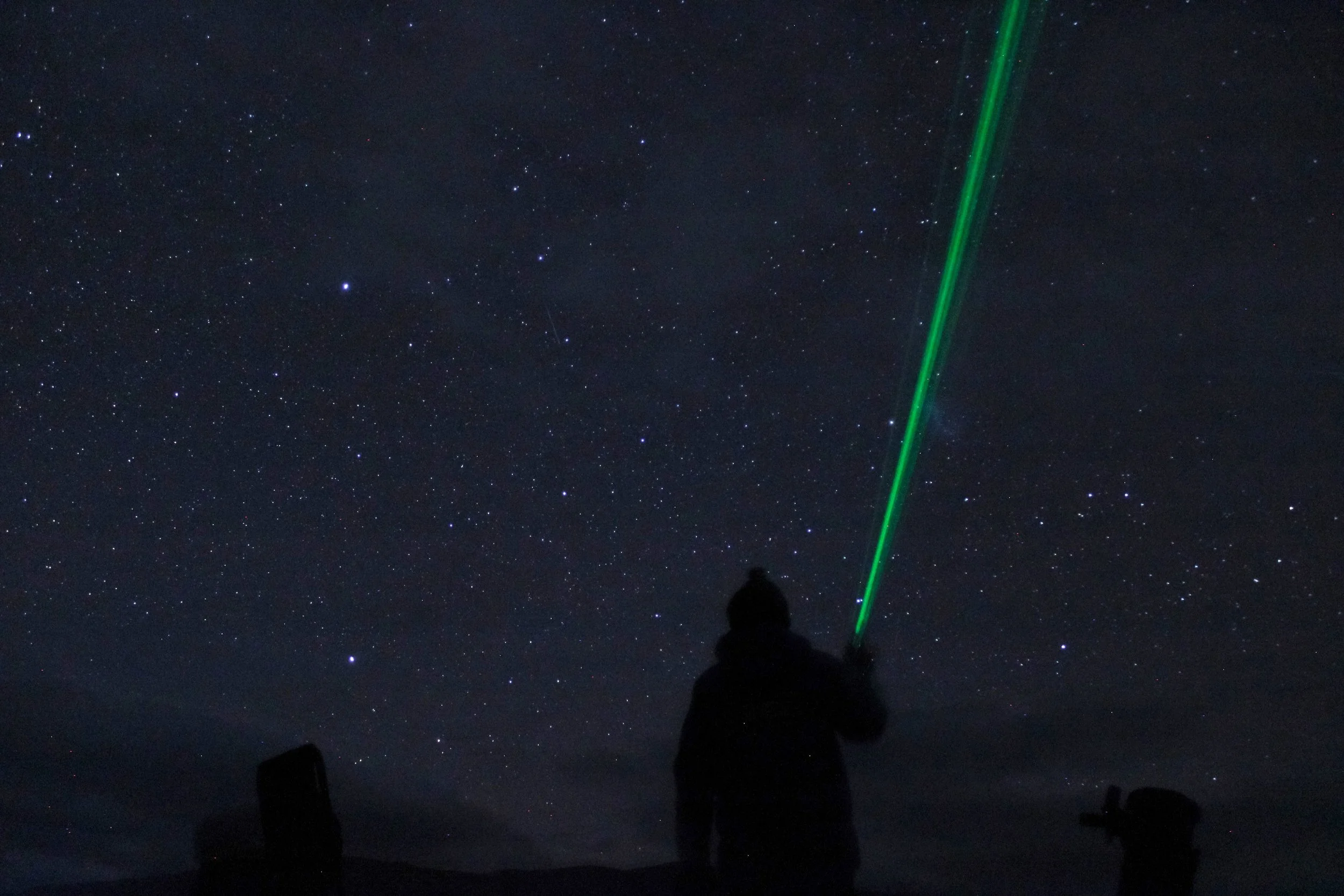 Person holding a green laser pointer, stargazing at a night sky filled with stars.