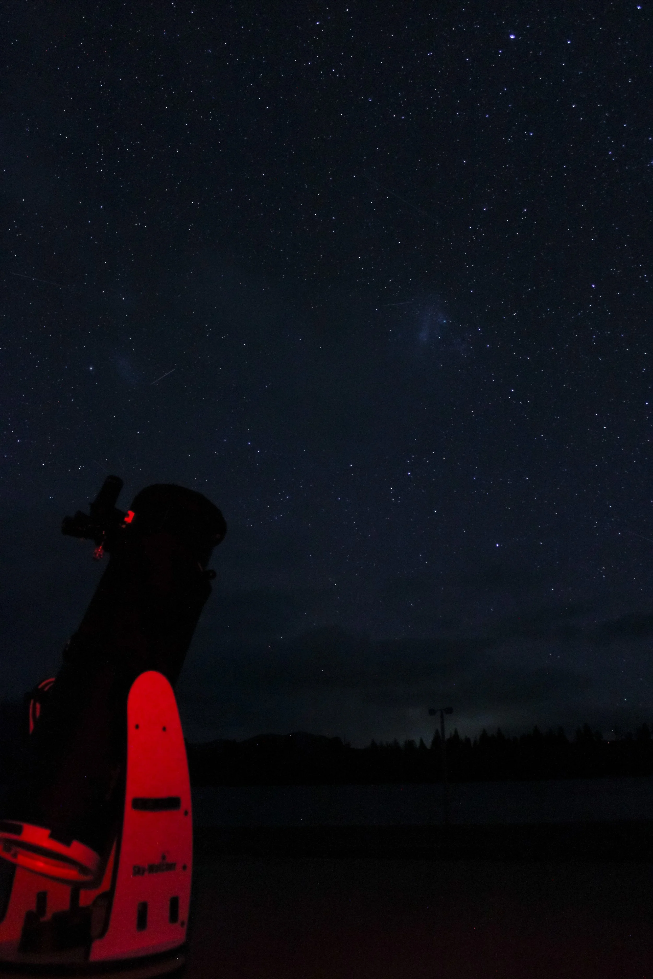 A telescope pointed toward a starry night sky with numerous stars and faint clouds or atmospheric haze in the background.