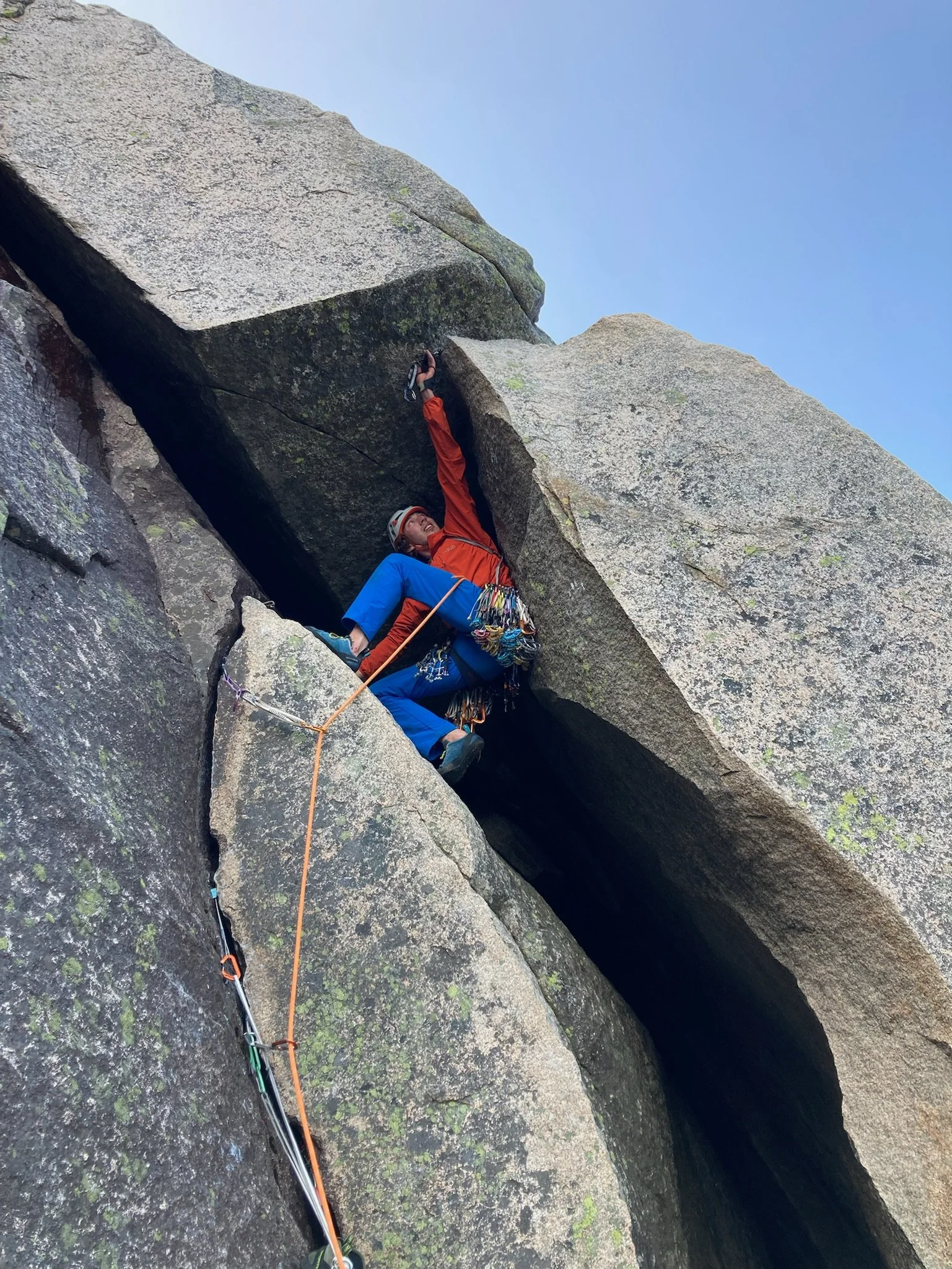 Climber reaching for a hold on a rugged rock face during a climb, equipped with climbing gear and safety ropes.
