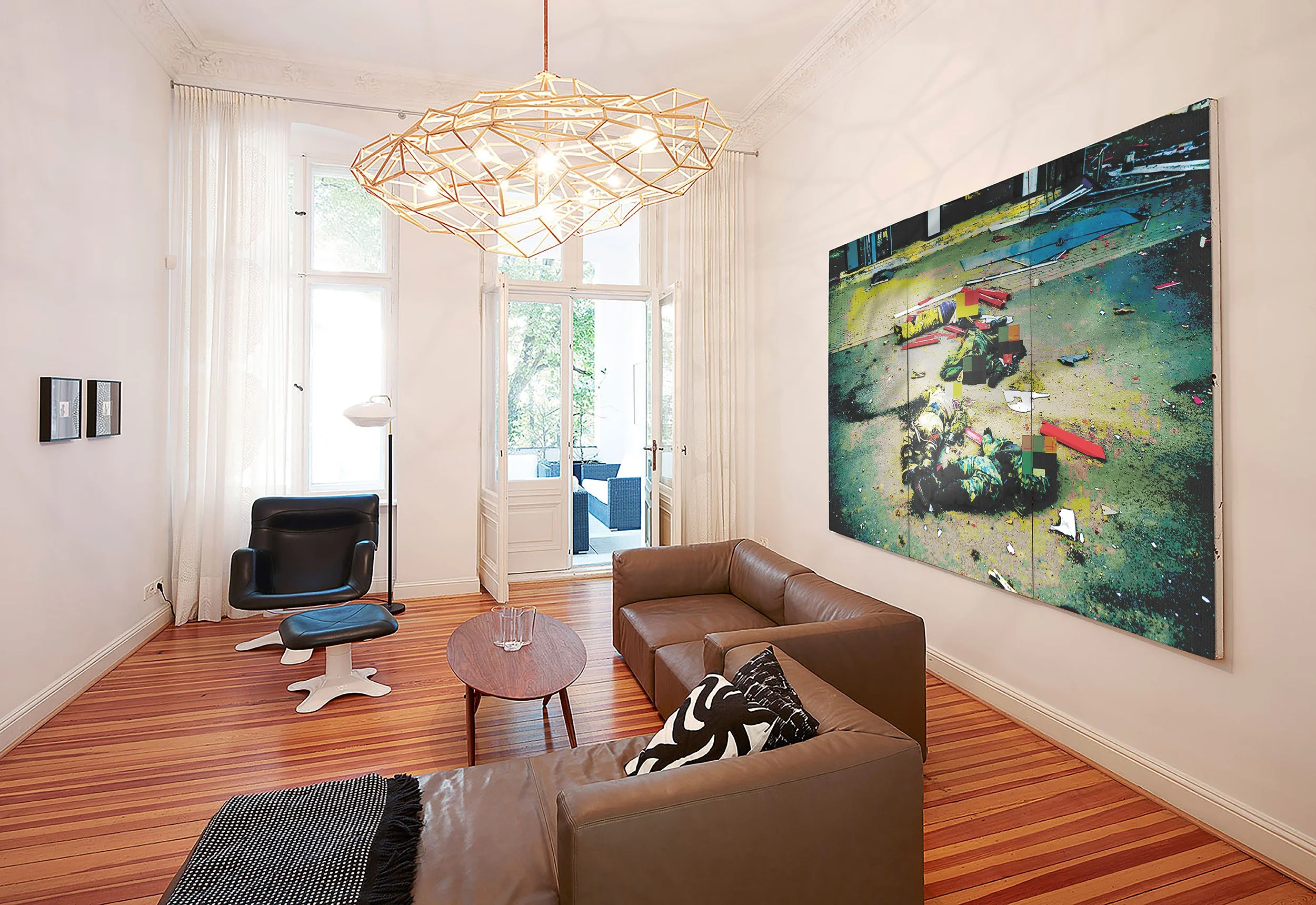 Living room with a brown sofa, black armchair with white legs, and a small wooden table with a glass pitcher. Large abstract painting on the wall, tall window with sheer white curtains, and a unique geometric pendant light hanging from the ceiling.