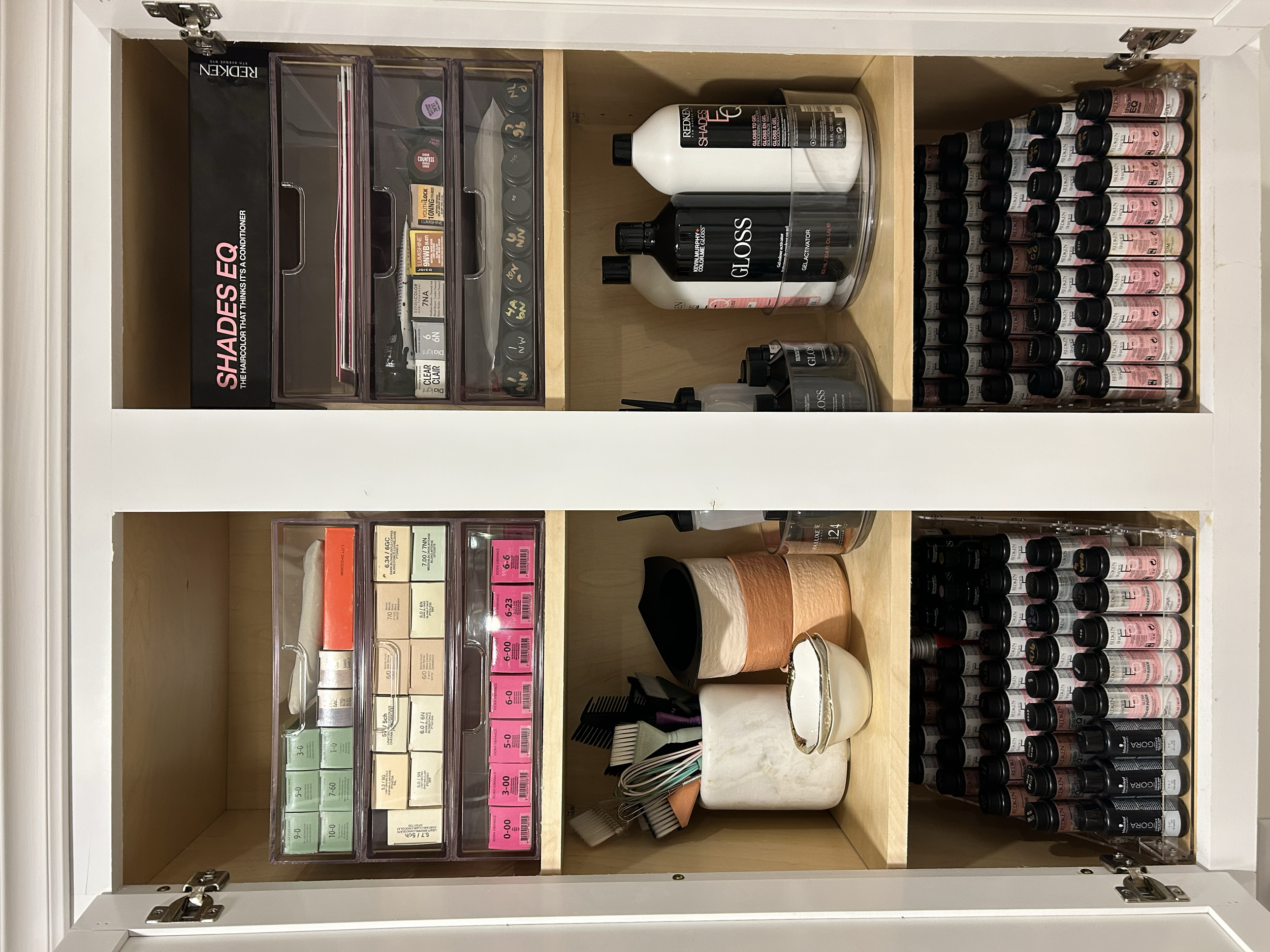 Organized open cabinet with various makeup and nail products, including nail polish bottles, brushes, containers, and organized boxes of beauty supplies.