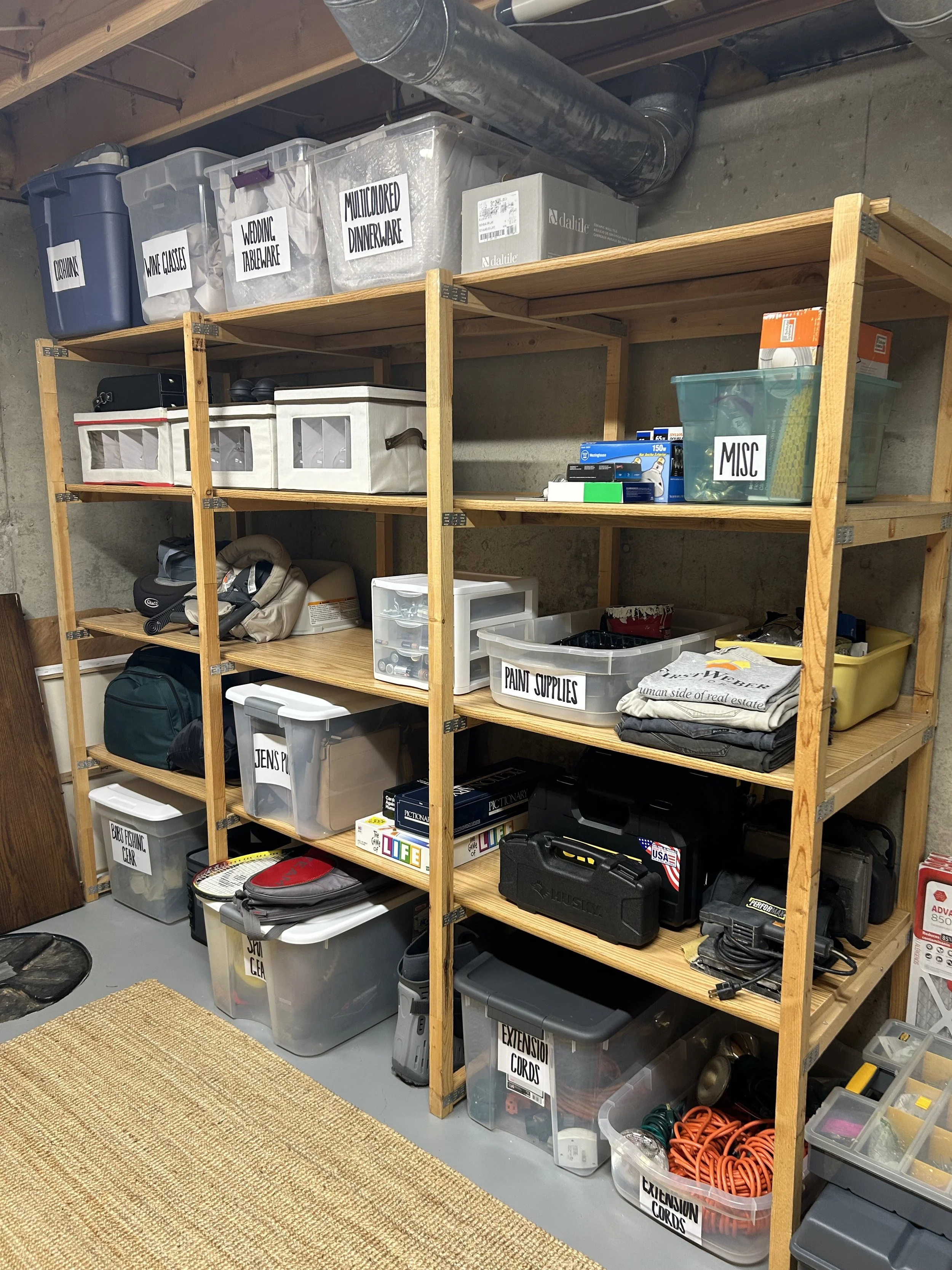 Wooden storage shelves filled with labeled plastic bins and items in a basement or garage.