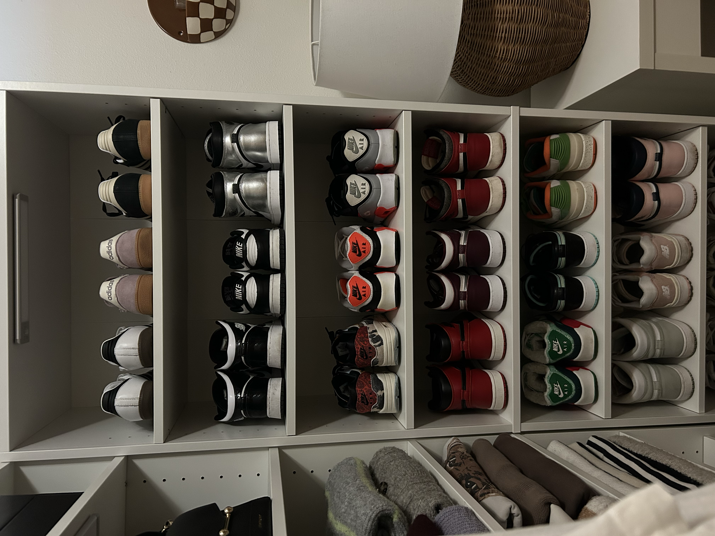 Multiple pairs of sneakers organized on open shelves in a closet, with various colors and styles including Nike, Adidas, and other brands.