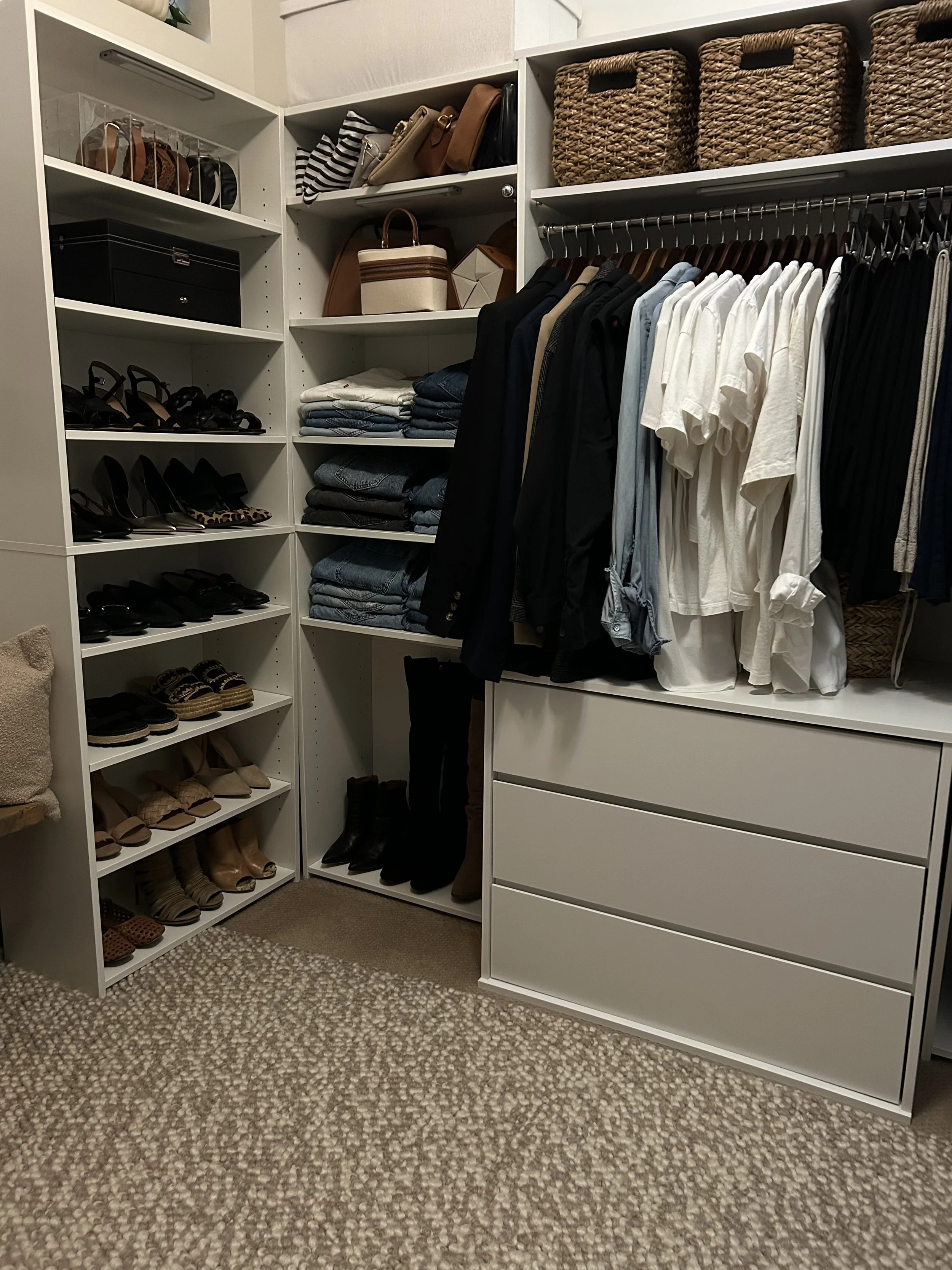 Organized walk-in closet with shelves of shoes, handbags, folded clothes, and hanging garments.