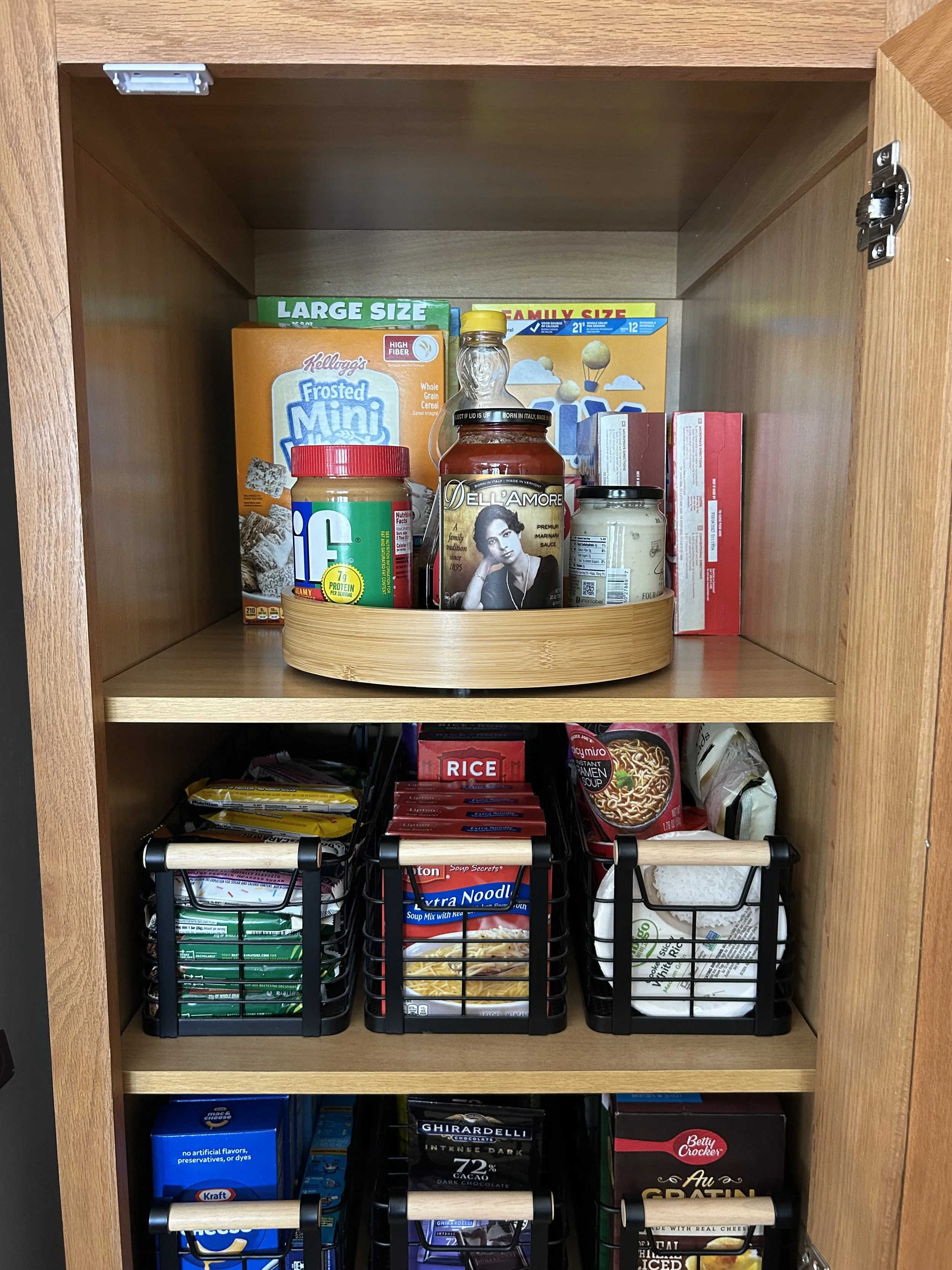 Open kitchen cabinet with snacks and food items inside, including cereal, pasta, instant noodles, and chocolate.