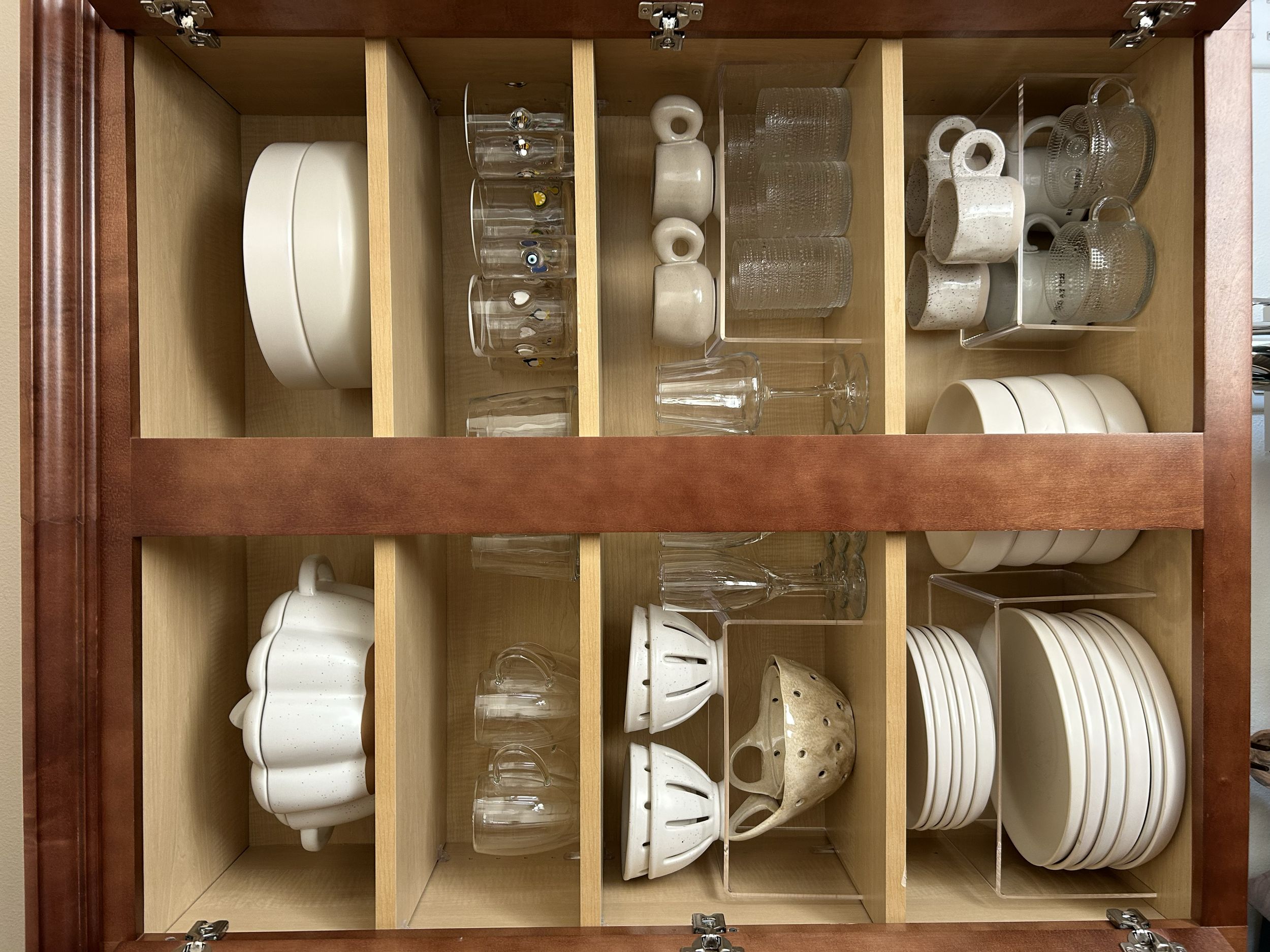 Open kitchen cabinet with dishware including white bowls, glasses, mugs, and small plates arranged on shelves.