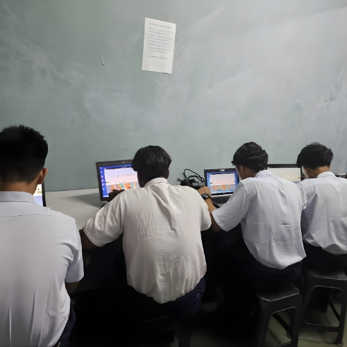 Four male students in white shirts working on computers in a classroom.