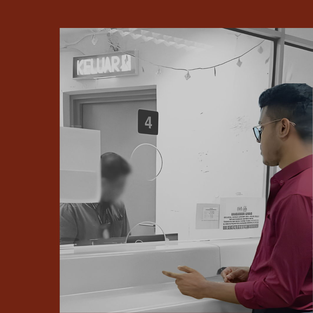 A man wearing glasses and a red shirt standing at a counter, interacting with a person behind a glass partition at a service desk with the number 4, in a room with a sign that says "KELUAR" and some signs and notices on the wall.