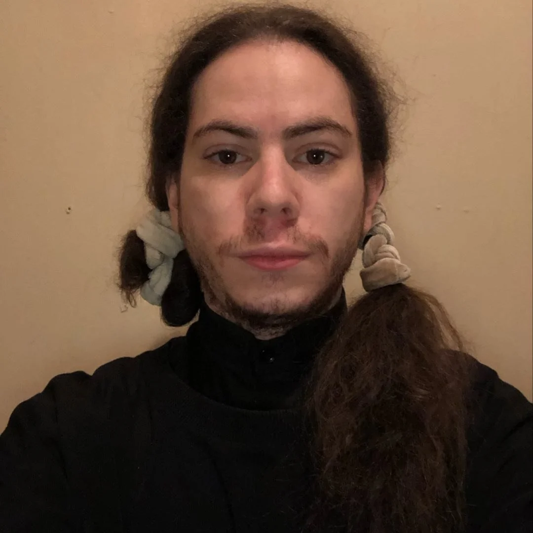 person with long hair styled in pigtails and wearing a black top, posing against a plain background