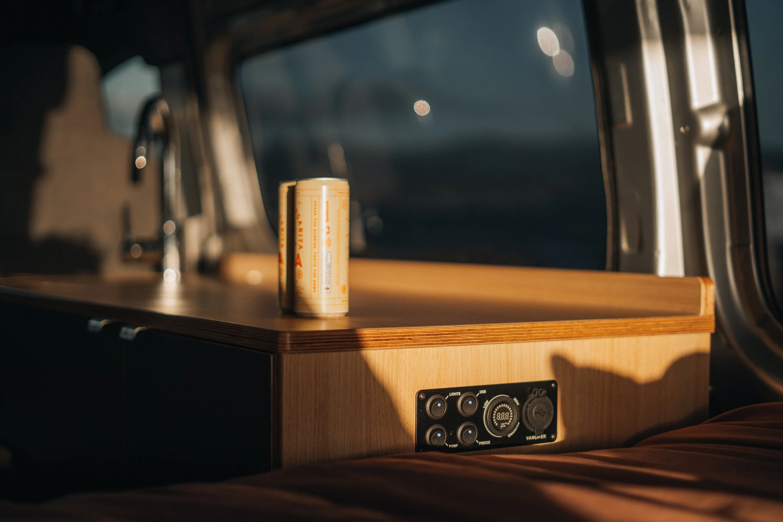Inside a vehicle, a small wooden table with a can of cream soda, sunlight casting shadows, and vehicle controls visible on the side panel.