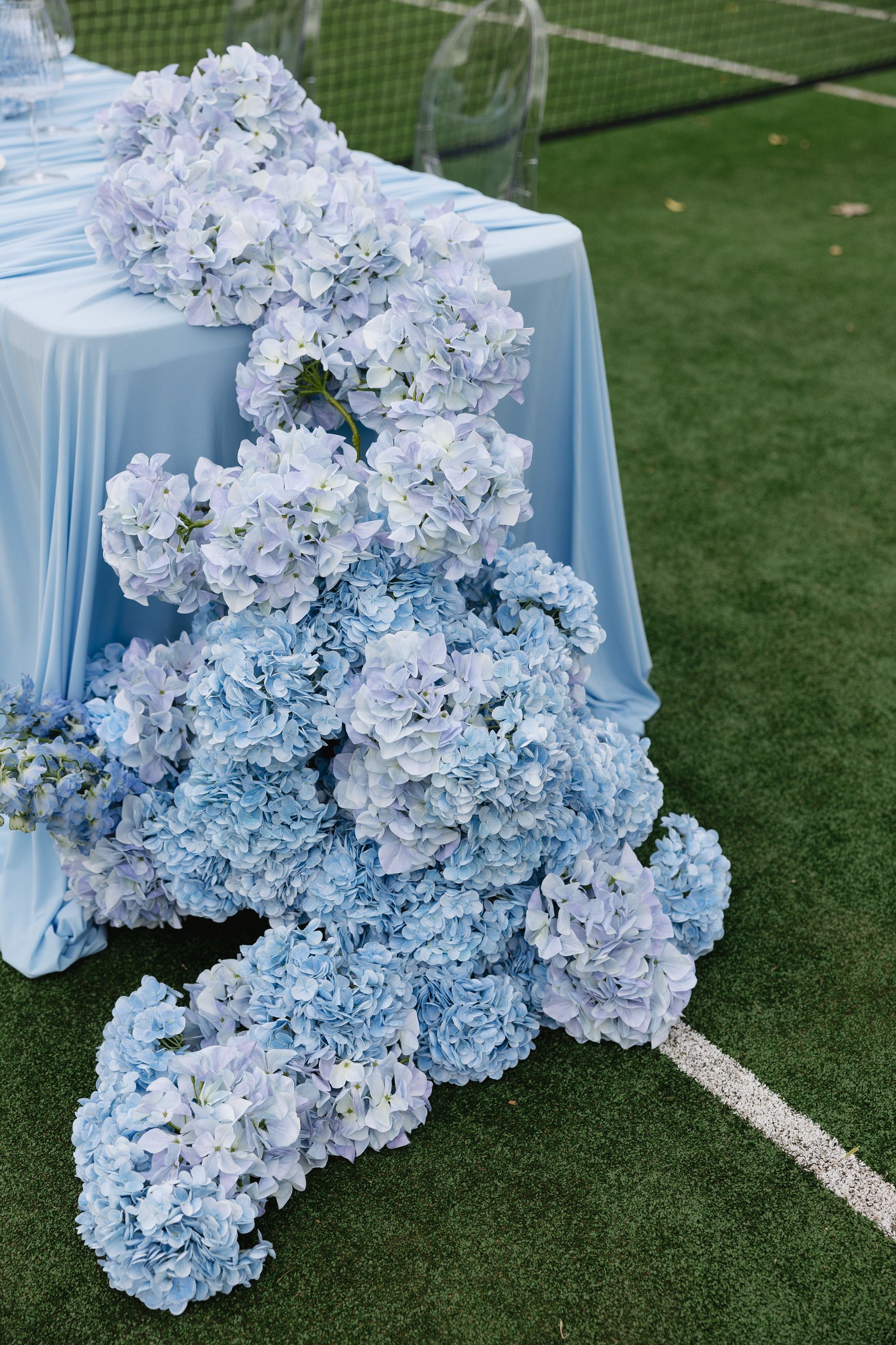 Blue and white hydrangea flowers arranged at a table on a tennis court.