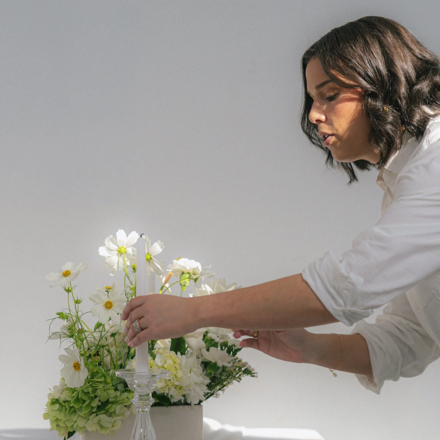 A Wedding Coordinator in Hunter Valley in a white shirt arranging white flowers on a glass candelabrum.