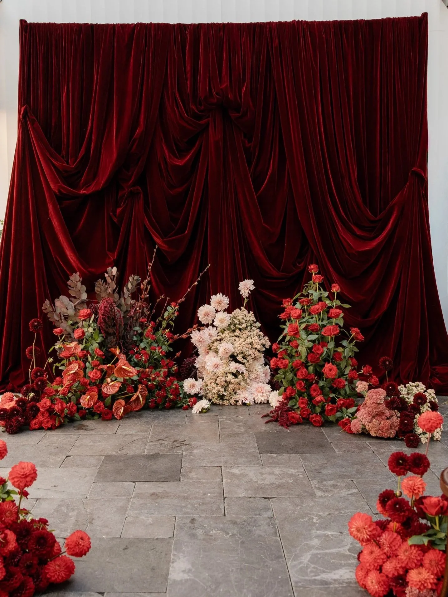 A backdrop of dark red velvet curtains with floral arrangements at the bottom, featuring pink, red, and white flowers.