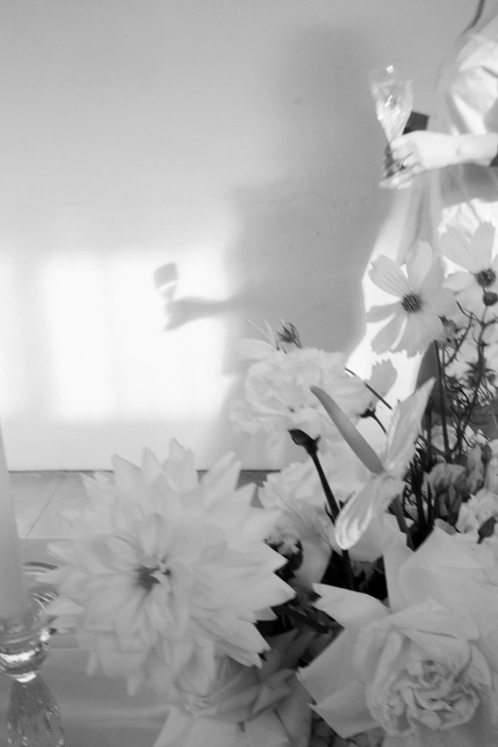 A close-up of a bouquet of flowers, possibly white lilies or daisies, with some in a vase and others scattered nearby, in black and white.