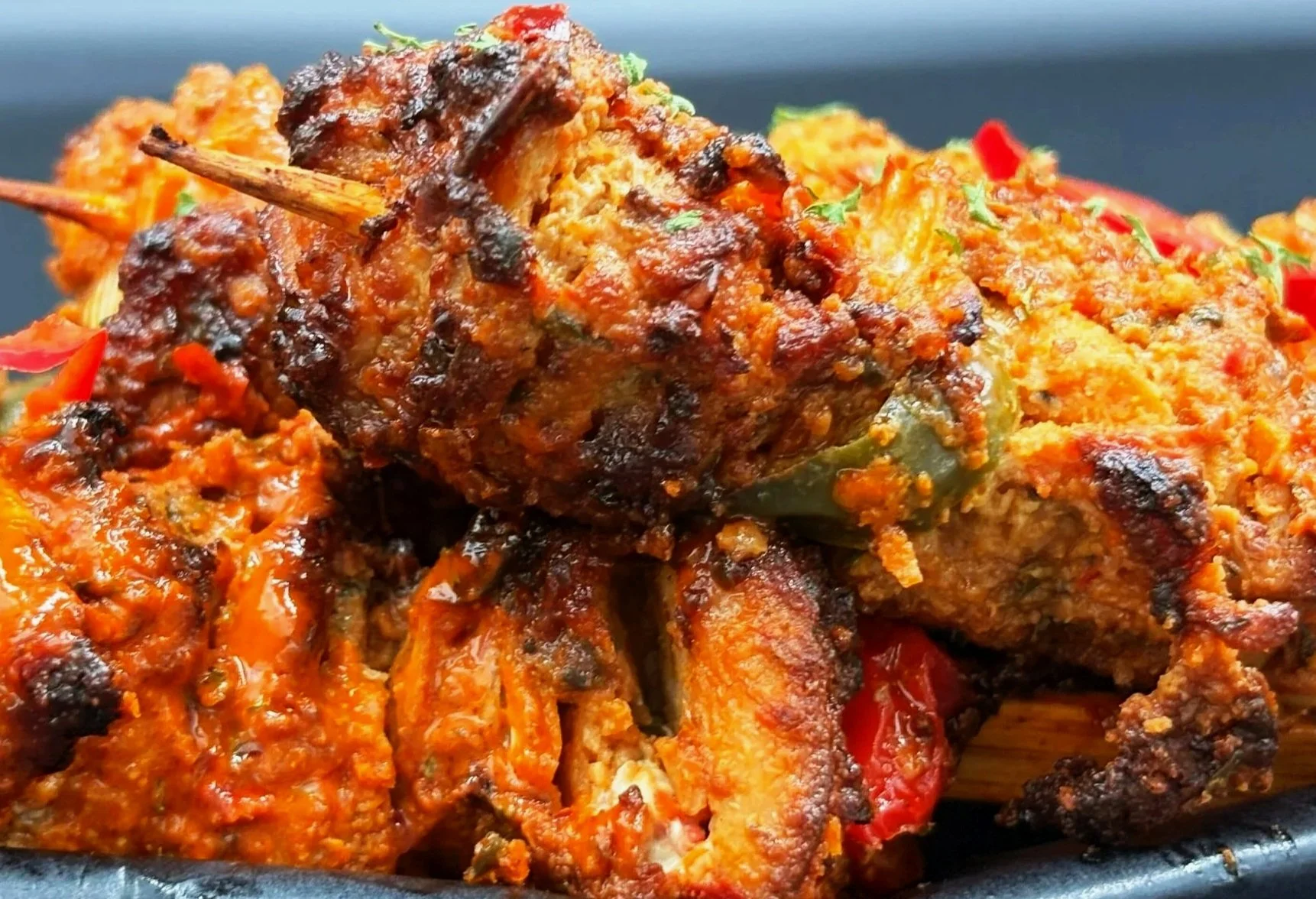 Close-up of grilled kebab with chopped vegetables and spices on a black plate.