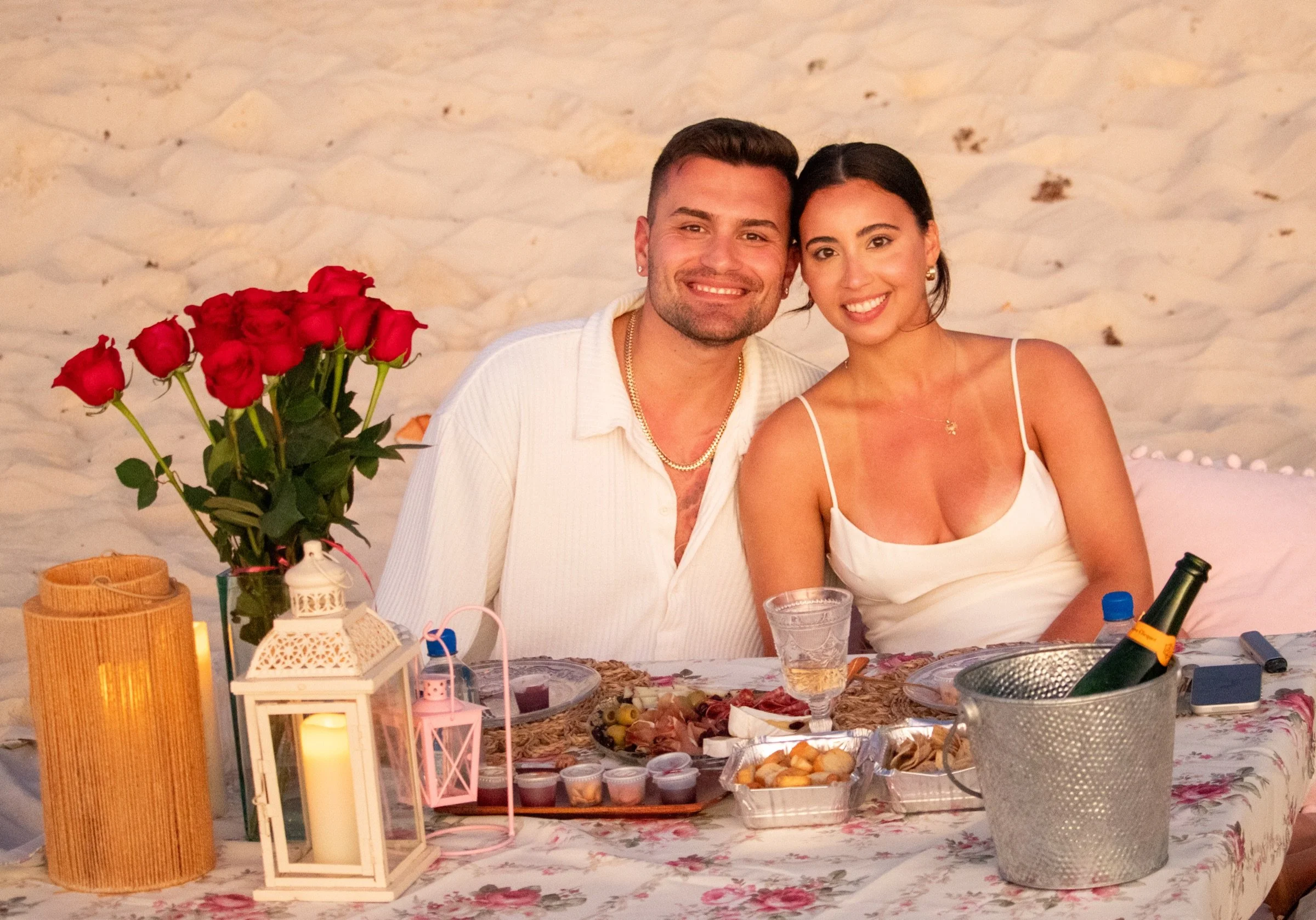 A couple celebrating together at a romantic picnic with red roses, candlelight and refreshments.