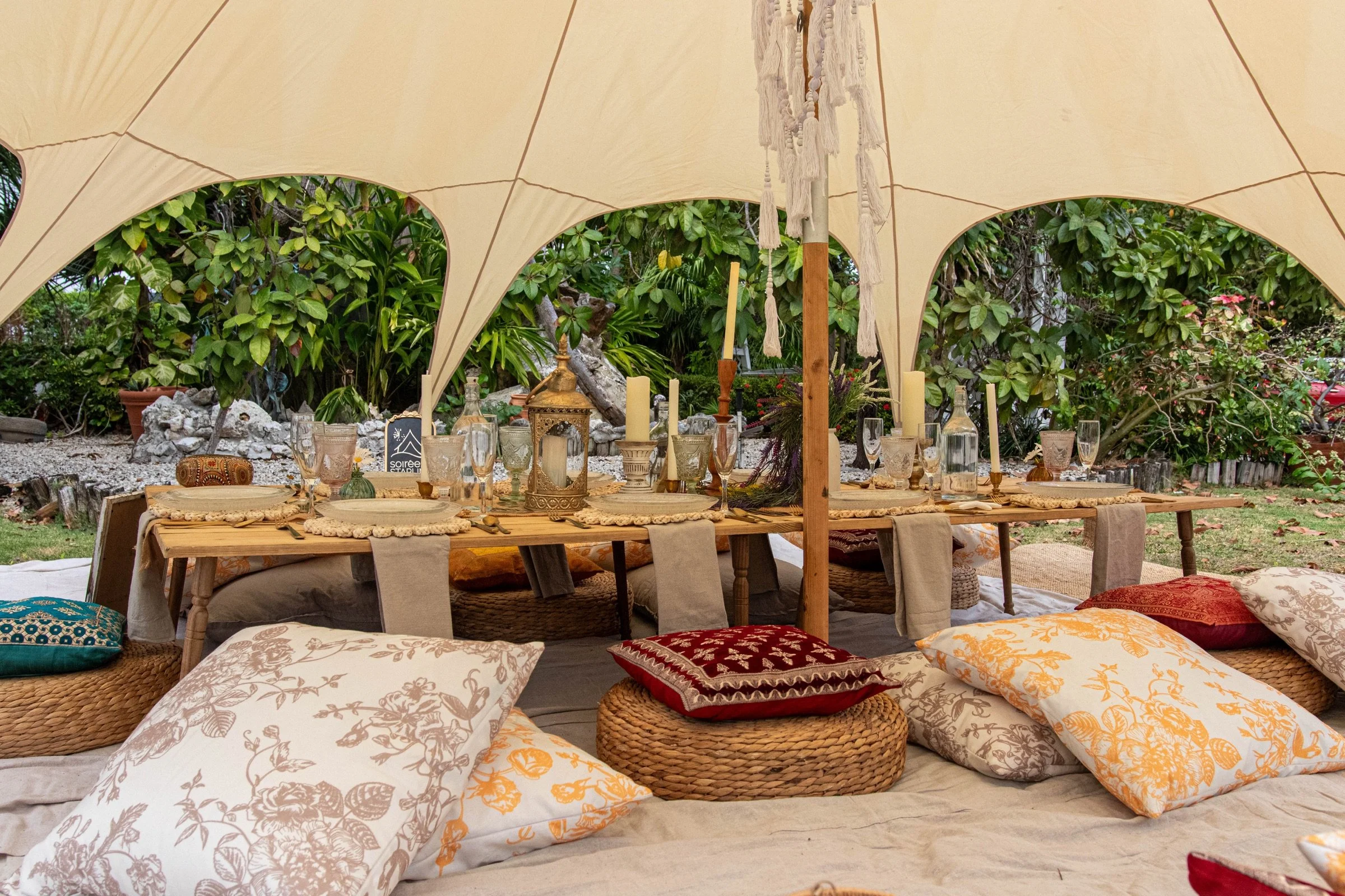 A spacious shaded picnic configuration with layered cushions and dining tables beside the beach.