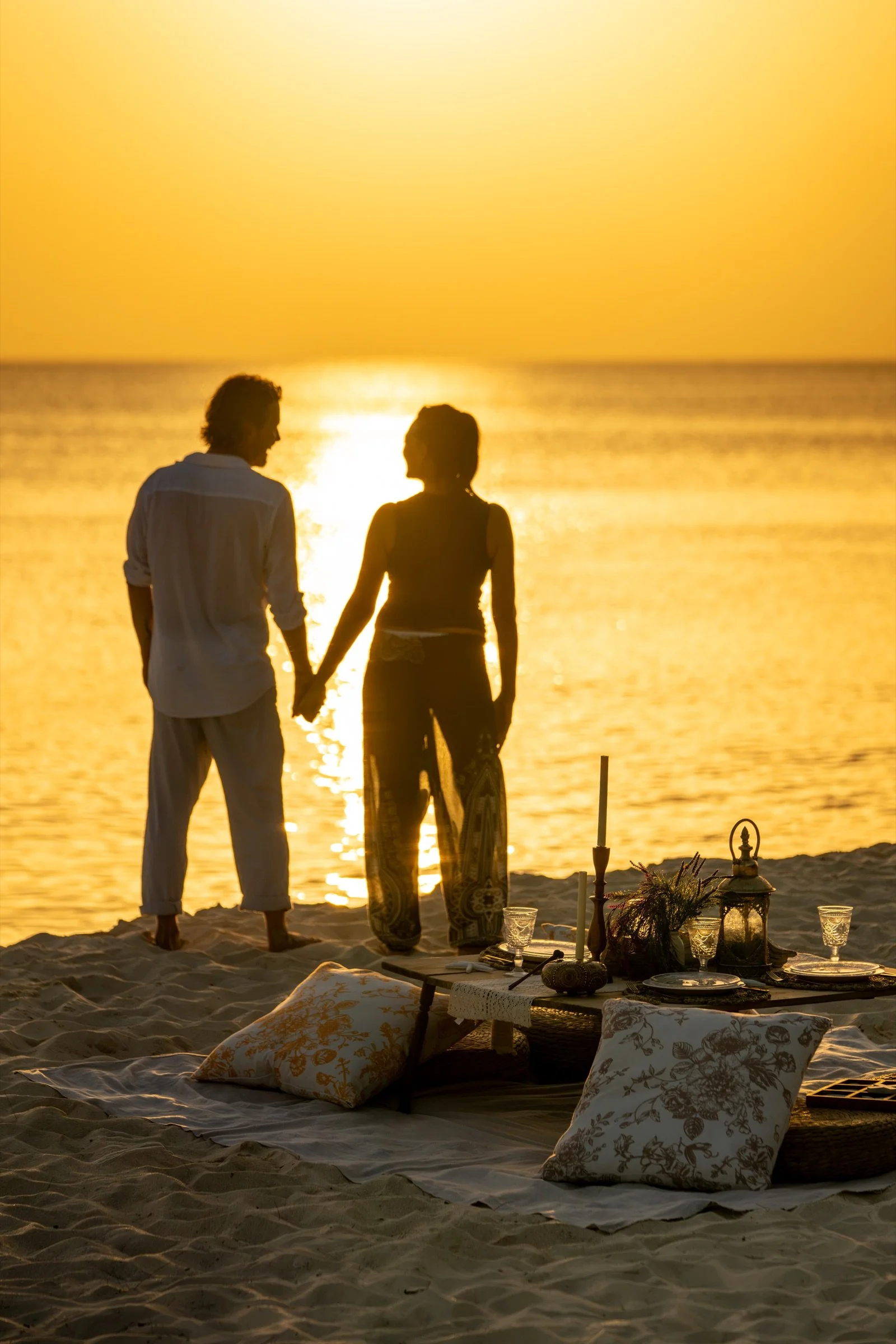 A couple sharing a golden-hour moment beside their intimate Cayman beach picnic.