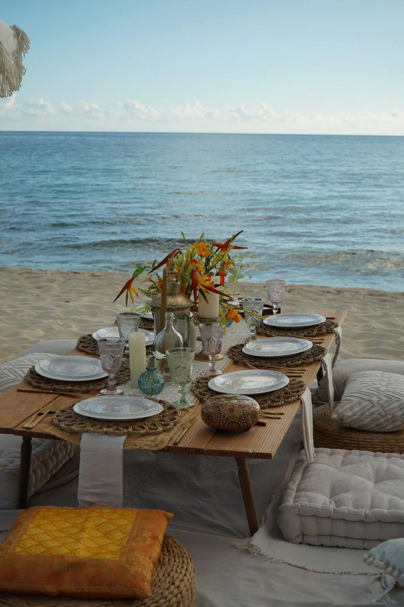 A bright daytime beach picnic with flowers, tableware and soft neutral cushions.