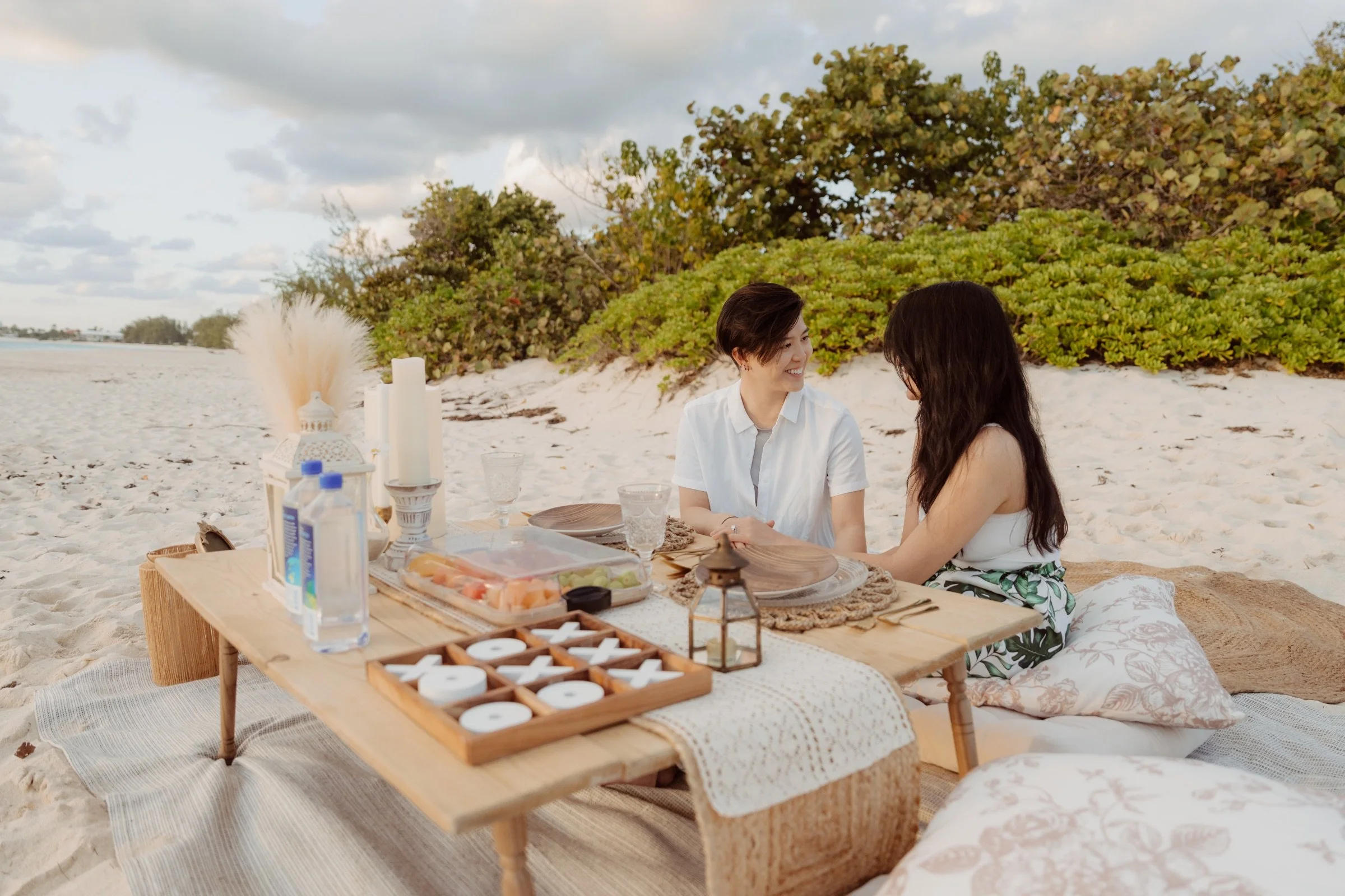 A couple sharing an anniversary picnic with charcuterie, candles and natural beach styling.