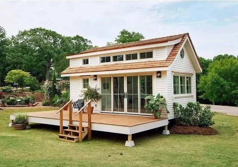 Custom-built tiny home with wood siding, large front deck, sliding glass doors, and modern roofline, designed for small house living in Maine.