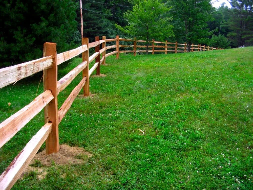 Split rail wood fence installation in Maine by local fence contractor, built on a slope with pressure-treated posts and rough-cut rails – ideal for farms, large yards, and rural properties. Expert fence services near Fairfield, Waterville, and Maine