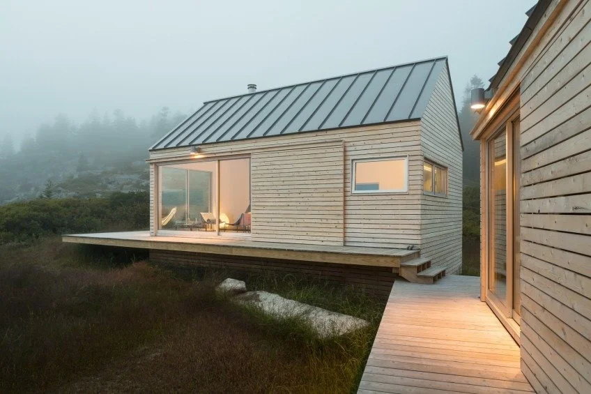 Modern custom-built small cabin with wood siding, metal roof, and large sliding glass doors, designed as a cozy retreat in rural Maine.