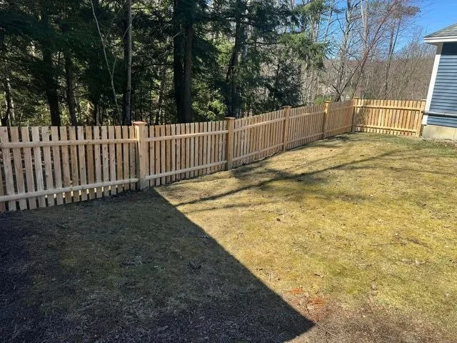 Wood picket fence installation in Maine by local fence contractor, built along a sloped backyard with pressure-treated posts and spaced vertical pickets. Ideal for residential properties in Fairfield, Waterville, and surrounding Central Maine areas.