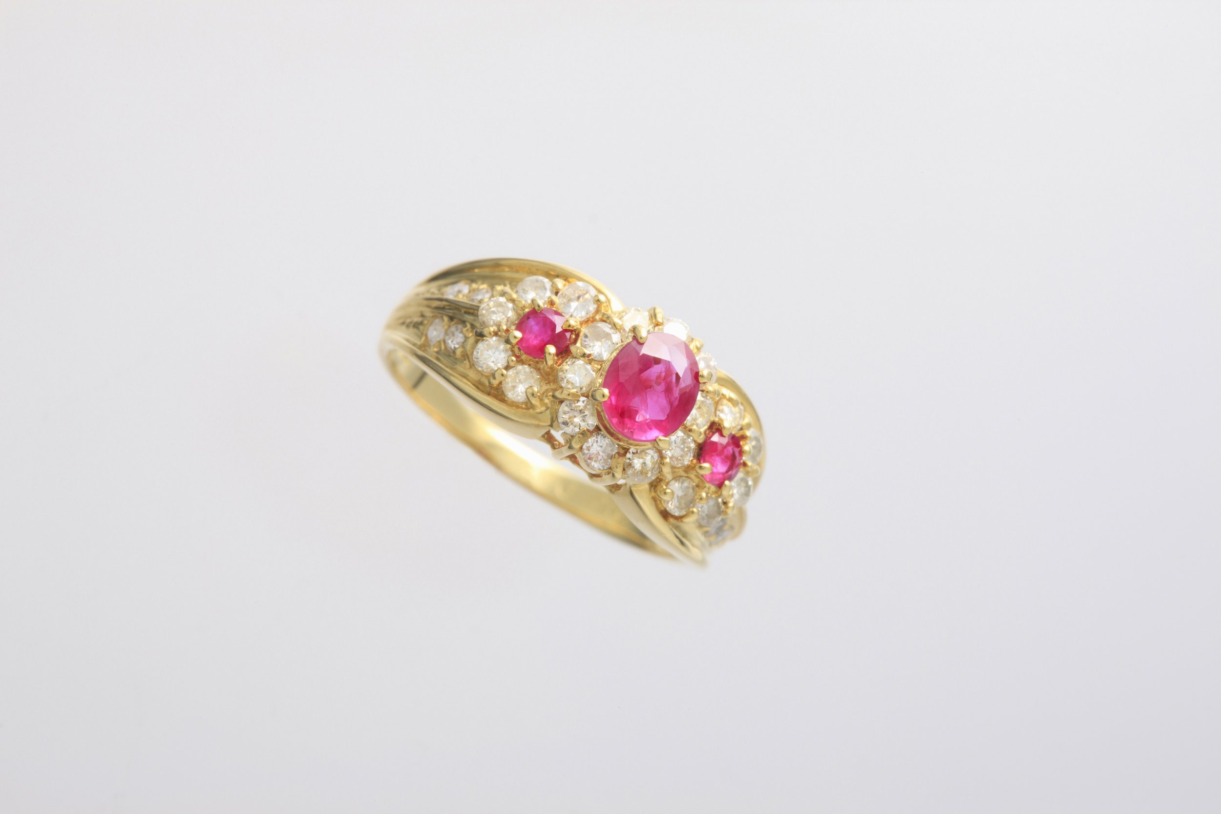 Gold ring with pink gemstones and surrounding clear diamonds on a plain gray background.
