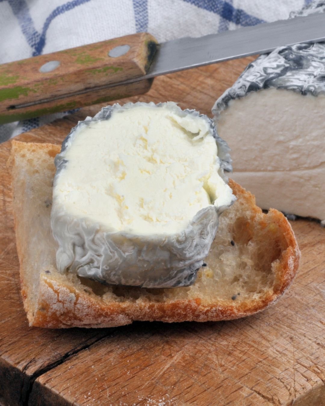 branza de capra. maturata in carbune taiata pe un fund de lemn langa un cutit si paine