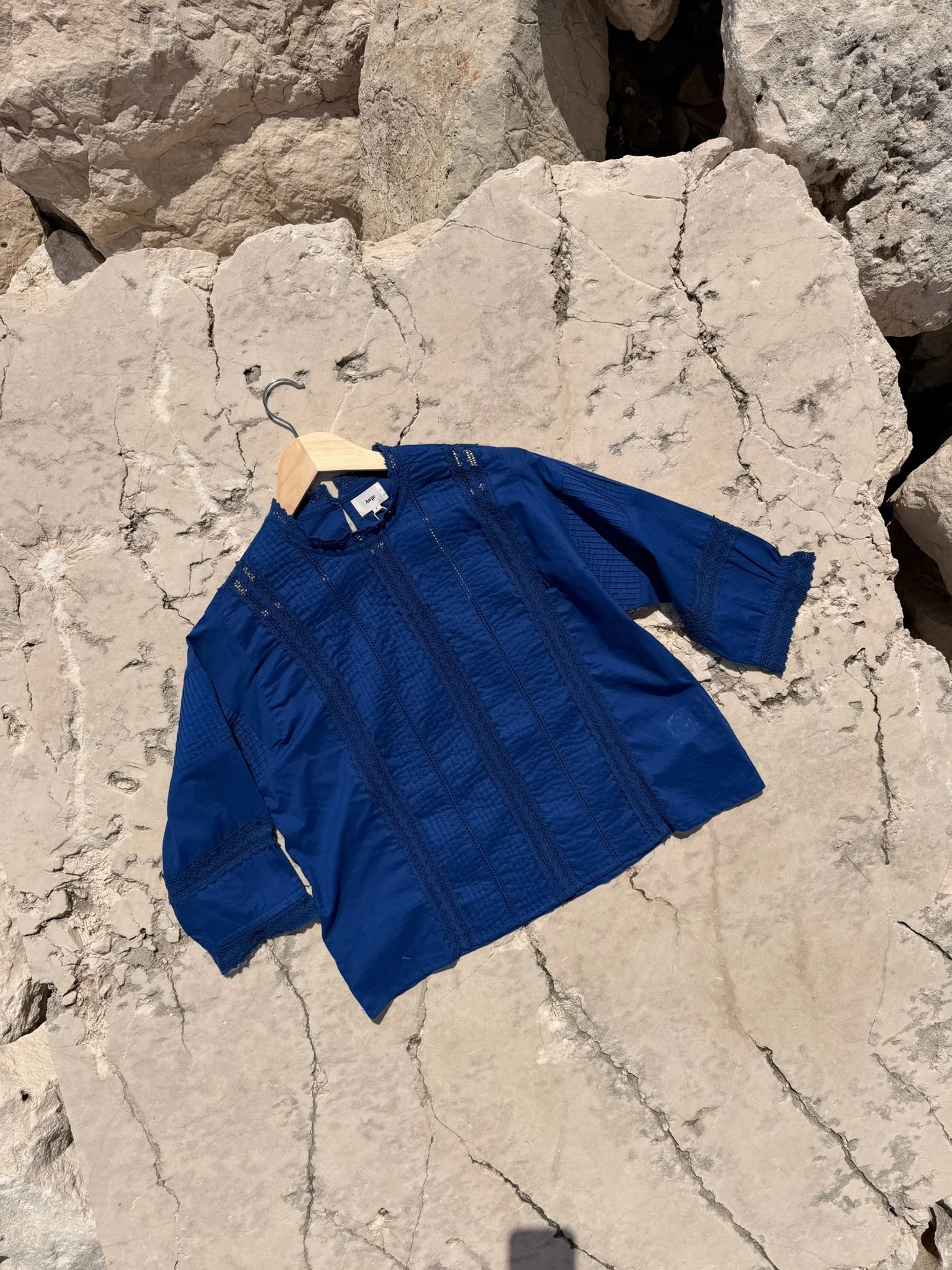 A blue jacket hanging on a wooden hanger placed on a large cracked white stone surface.