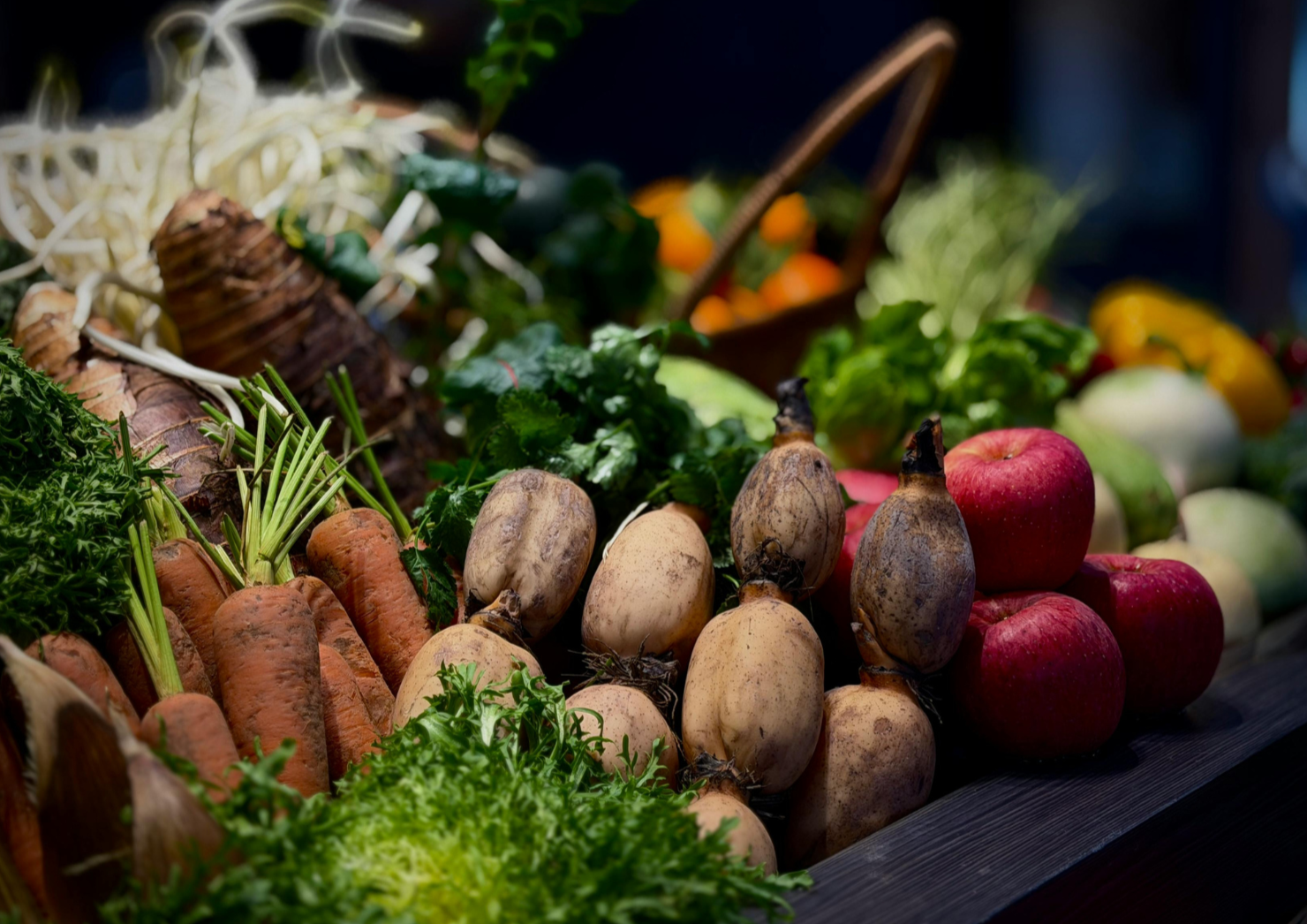 A display of fresh vegetables including carrots, beets, apples, and leafy greens at a market or farm stand.