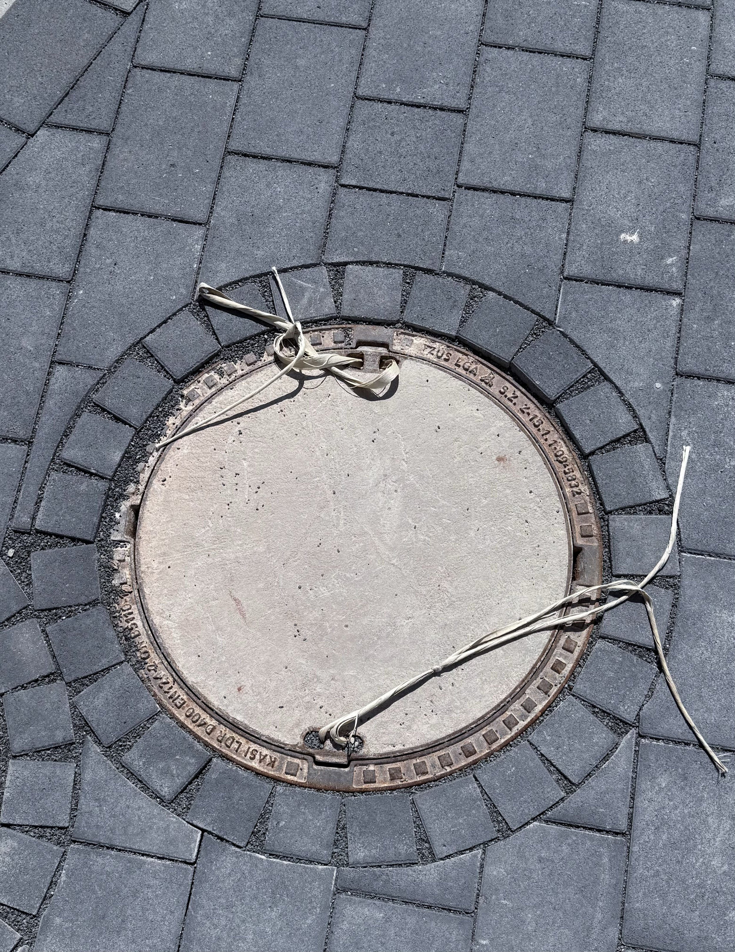 Offene Abdeckung eines Kanaldeckels im Boden, mit einem weißen Seil darum gewickelt.