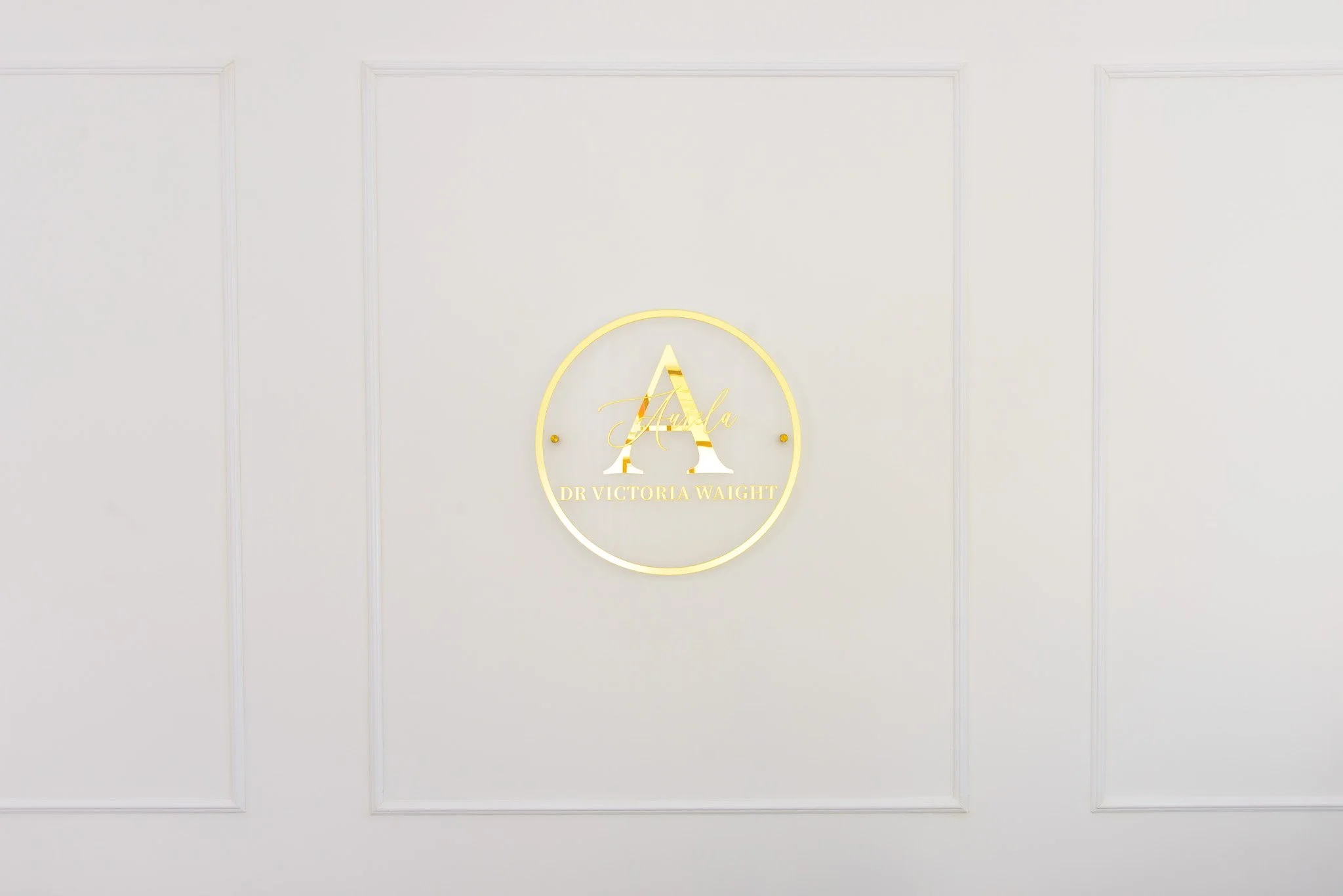 Gold sign on a white wall displaying the letter 'A' with the name 'Aurela' and the text 'Dr Victoria Waight' underneath.