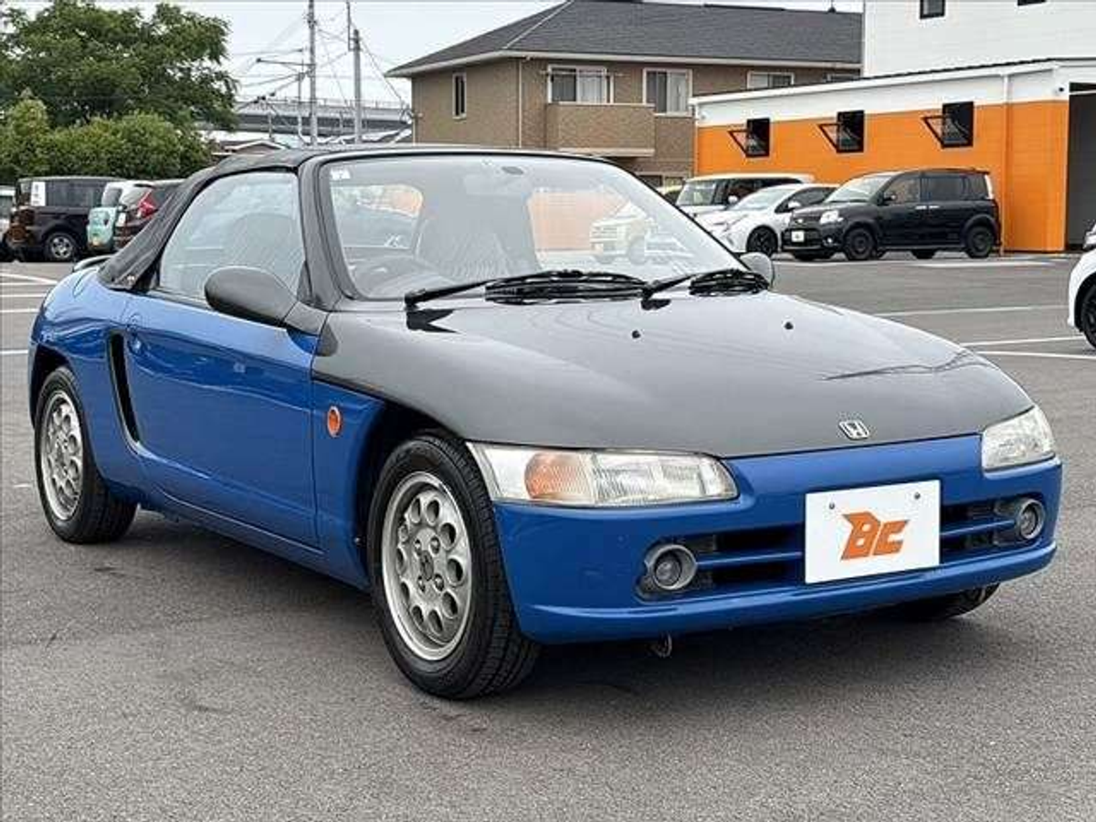 A blue and black Honda Beat convertible parked in a parking lot.