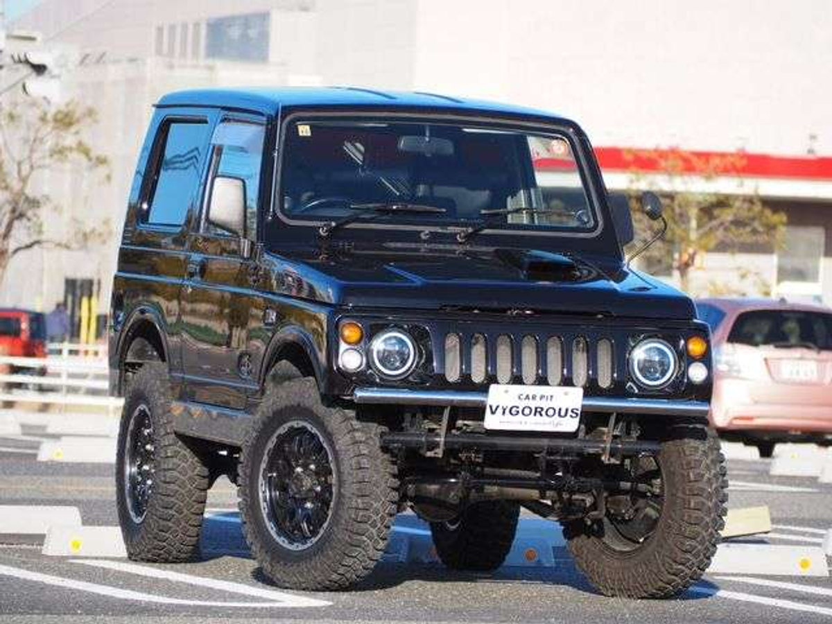 Sazuki Jimney, Black modified off-road  setup with large tires and custom rims parked in a lot.