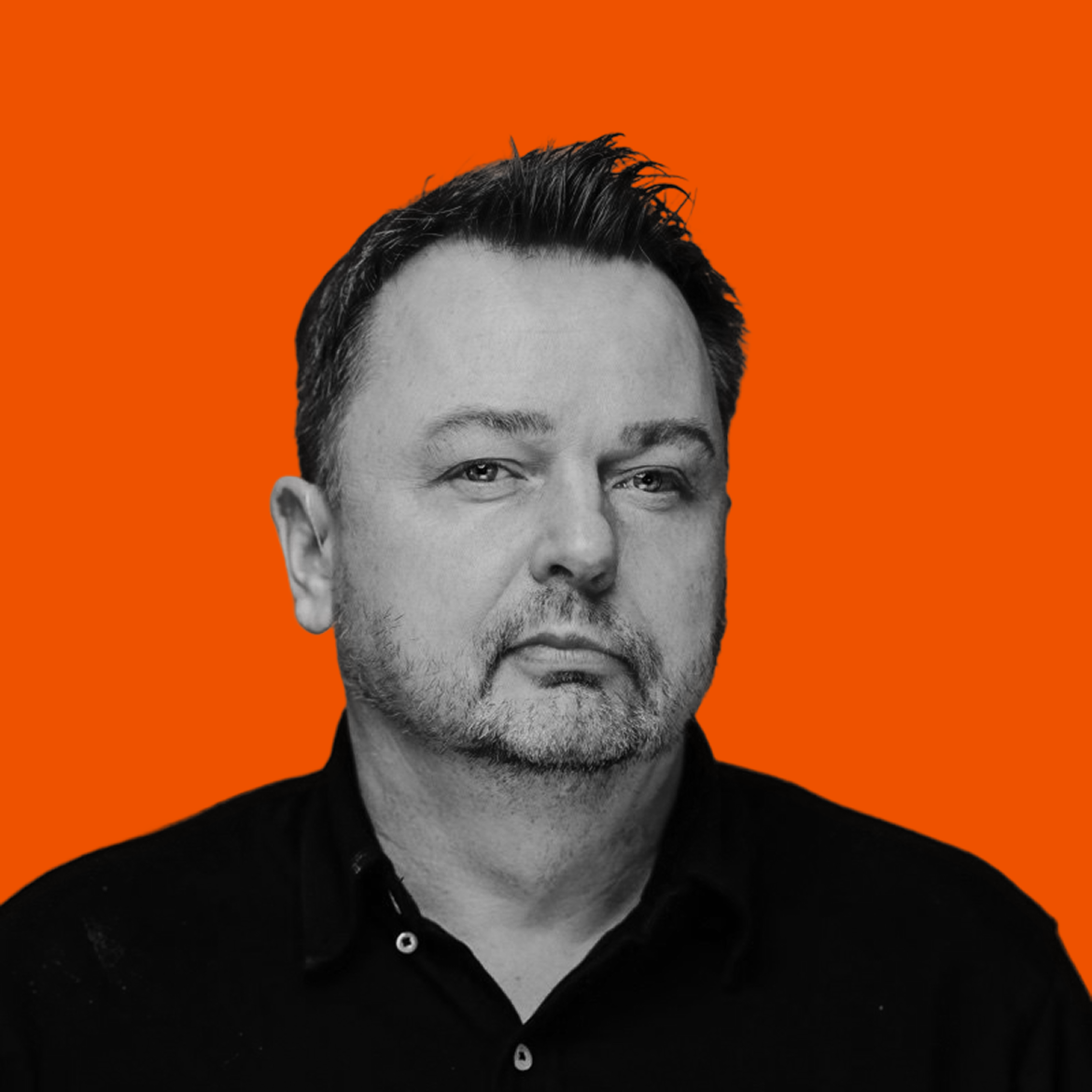 Black and white portrait of a middle-aged man with short dark hair and facial hair, wearing a dark collared shirt, against an orange background.