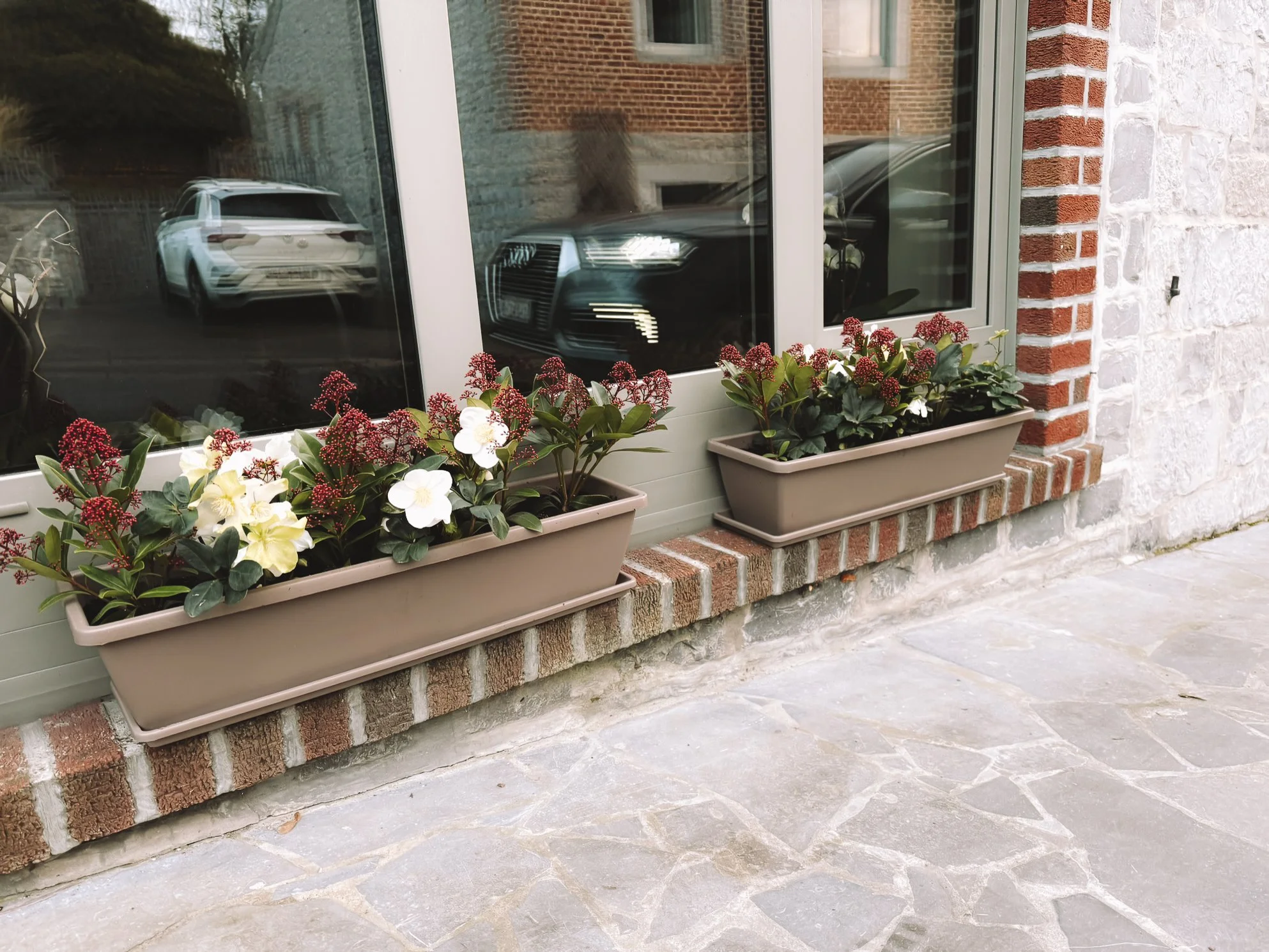 Twee plantenbakken met bloemen voor een raam van het vakantiehuis.