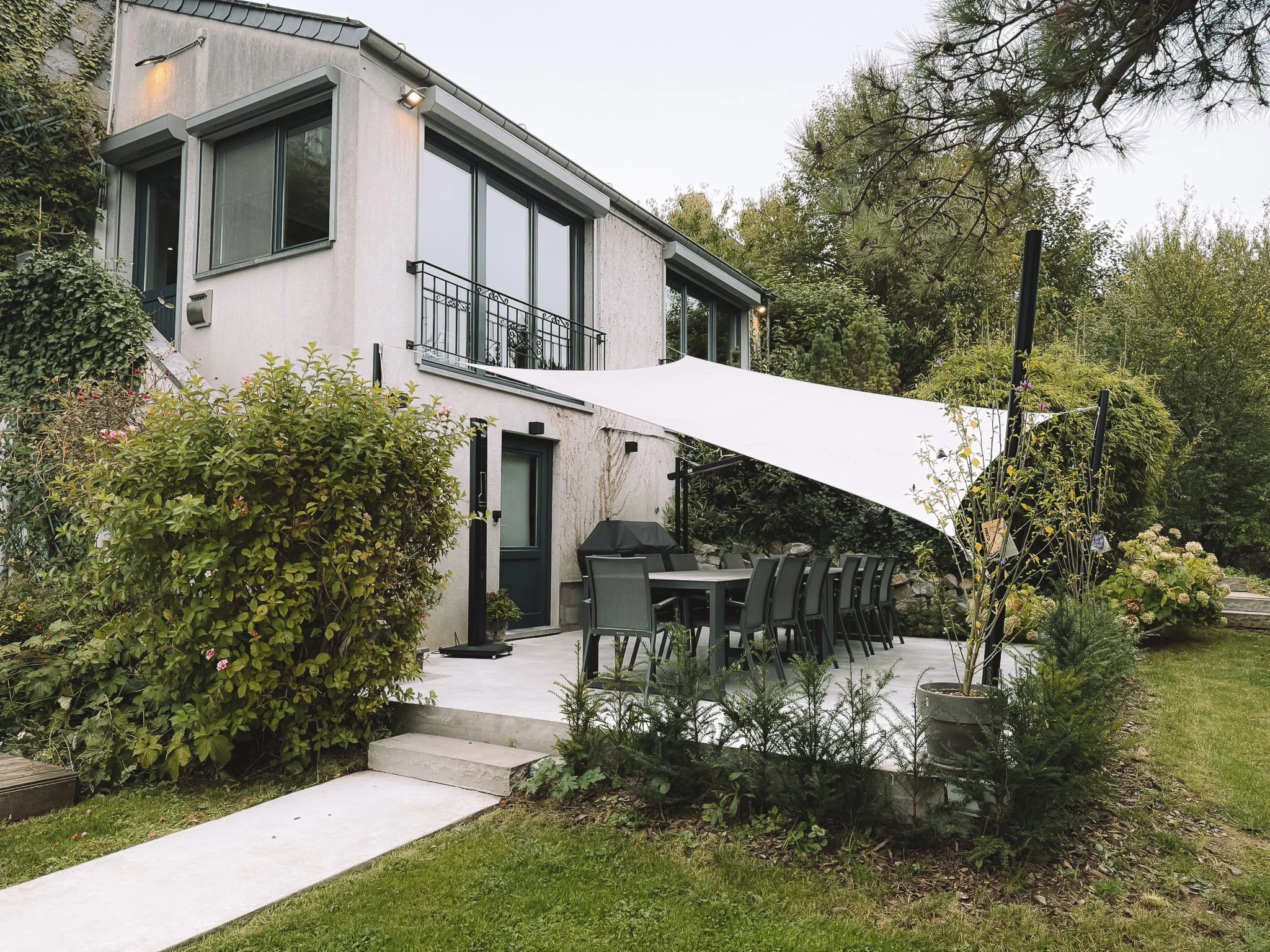 Een tuin met een terras en buitenmeubilair onder een wit schaduwdoek.